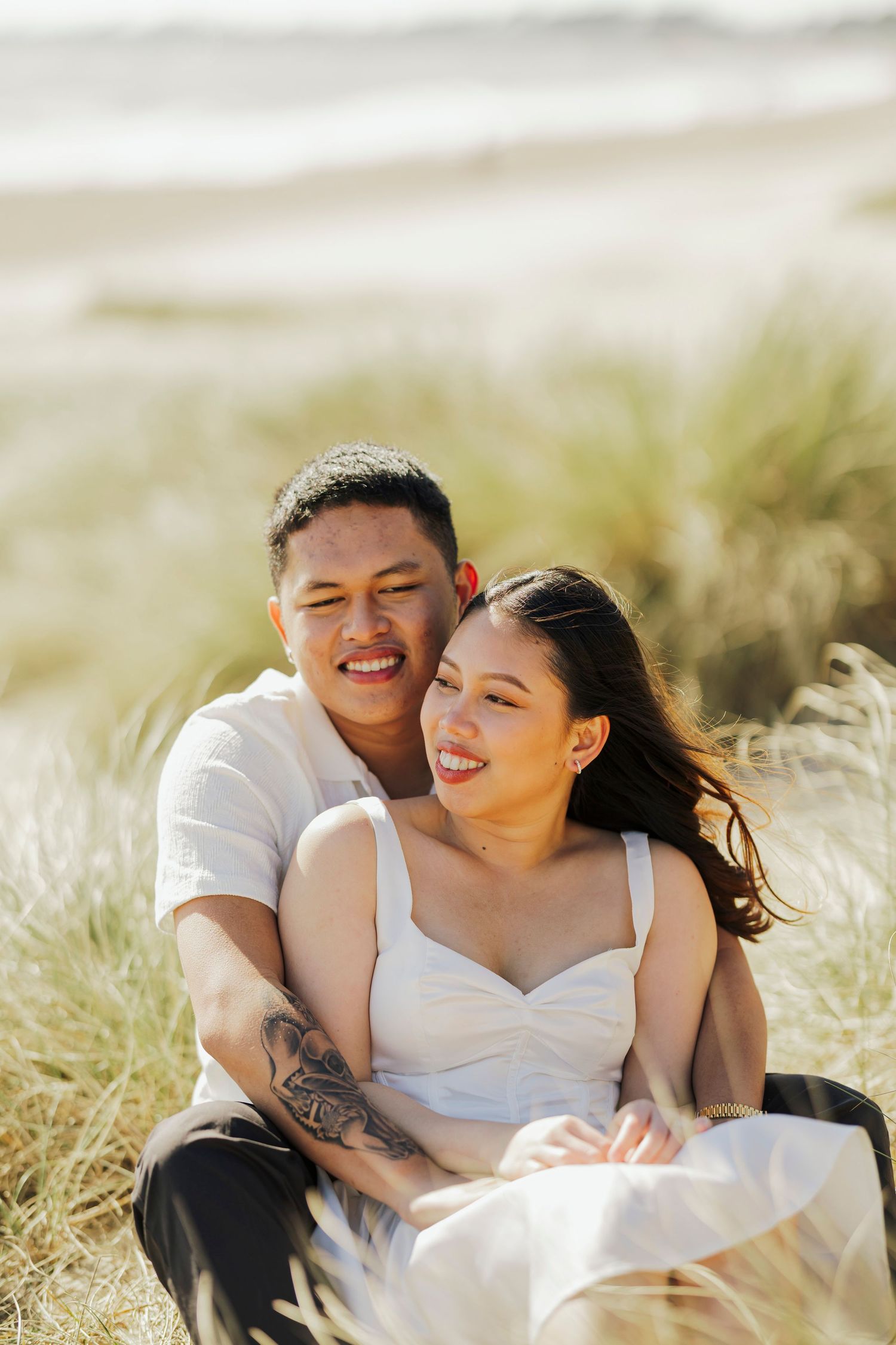 A happy couple sitting together in tall grass on a sunny day, laughing and embracing in natural lighting.