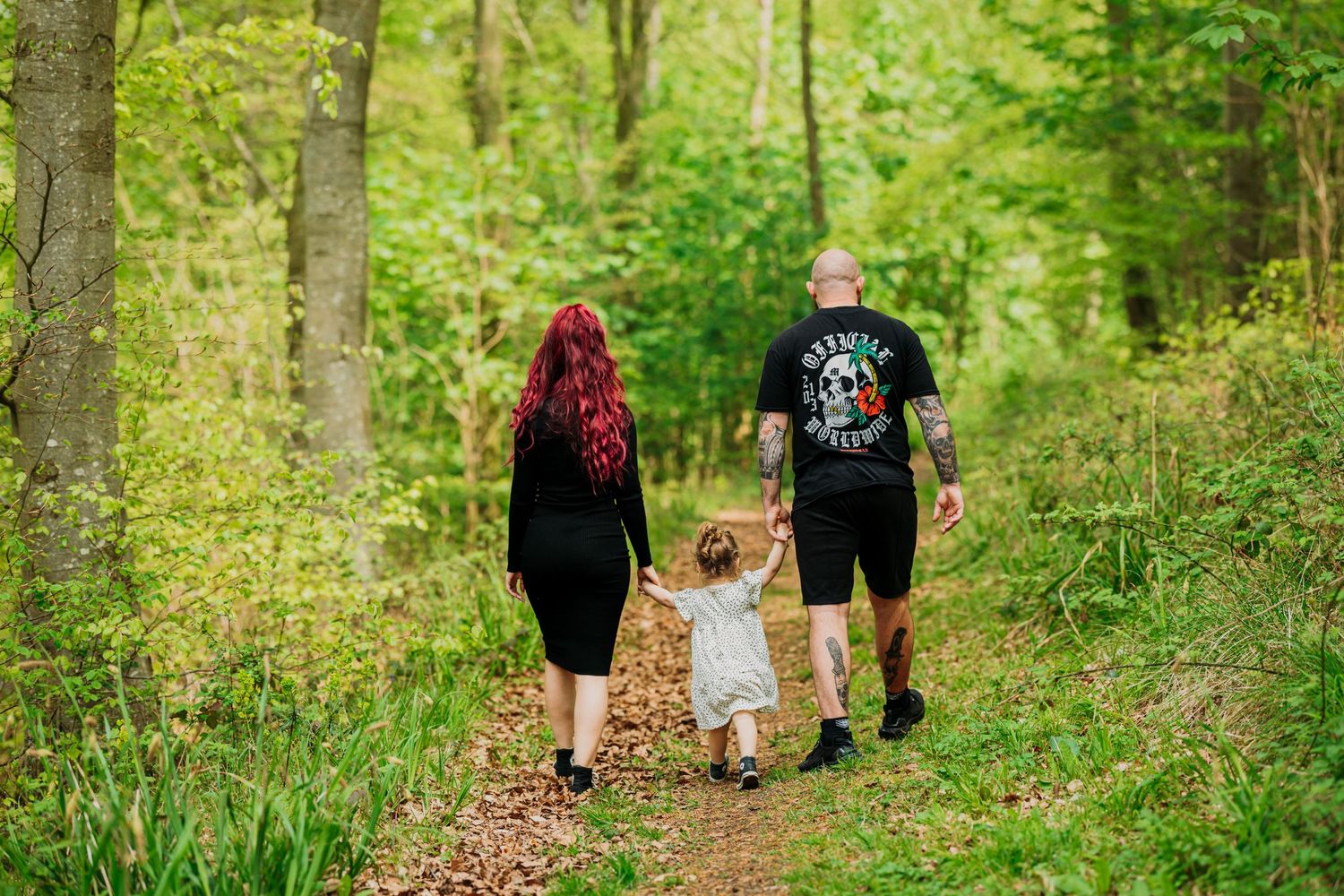 Family walking hand in hand down forest path surrounded by greenery.