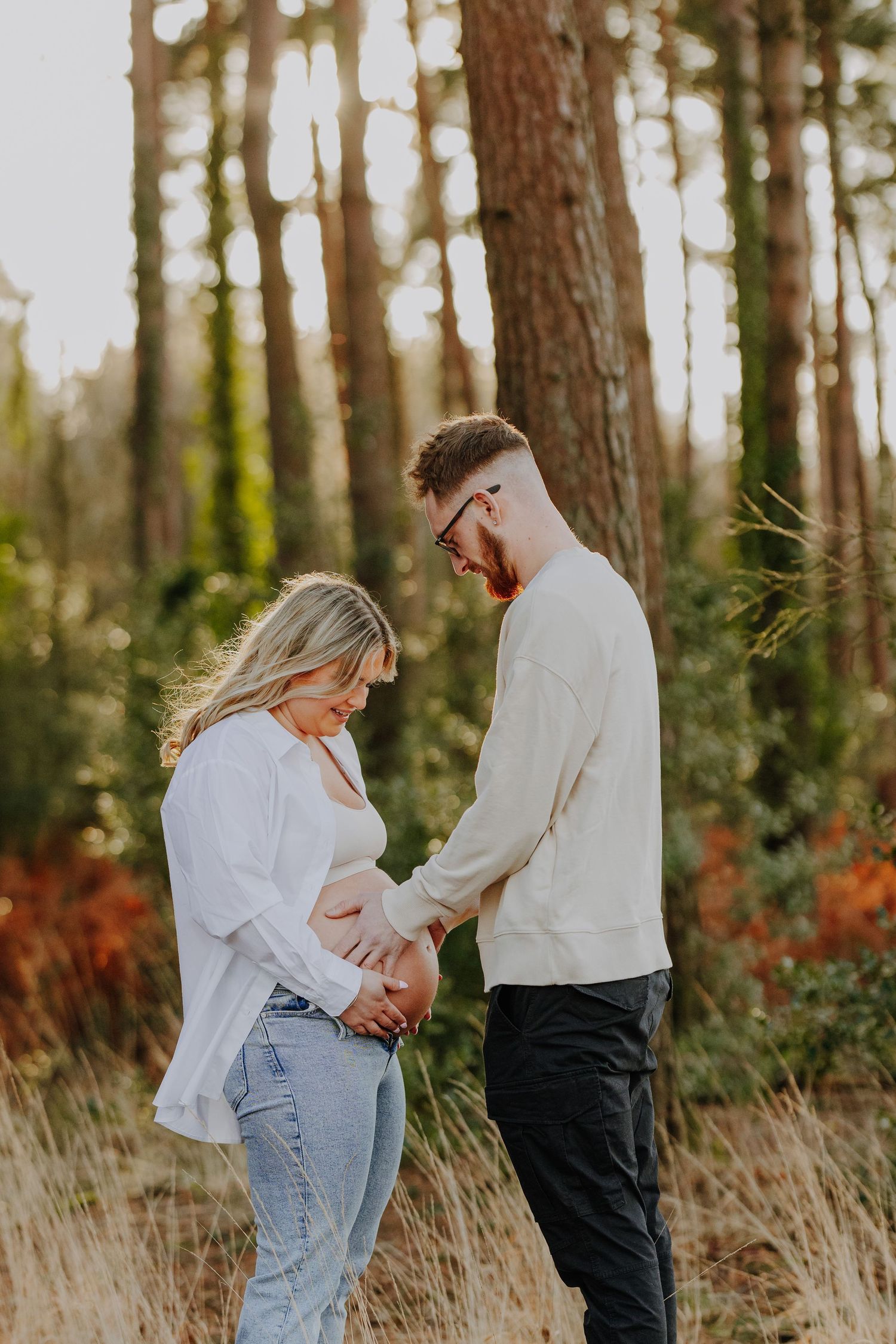 Couple sharing intimate moment during maternity photoshoot in pine forest.