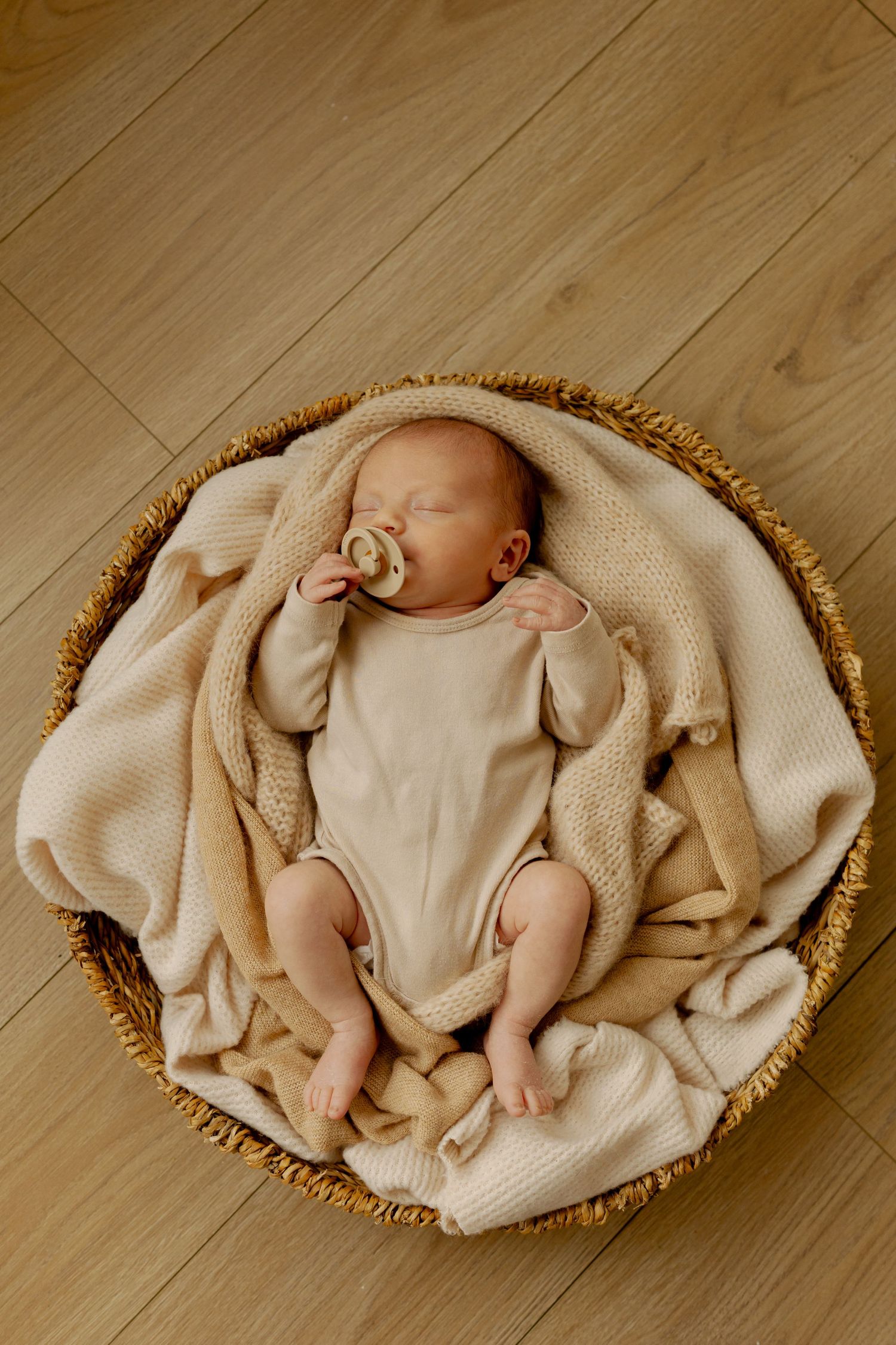A series of connected images showing a sleeping baby wrapped in beige fabric on a wooden floor.