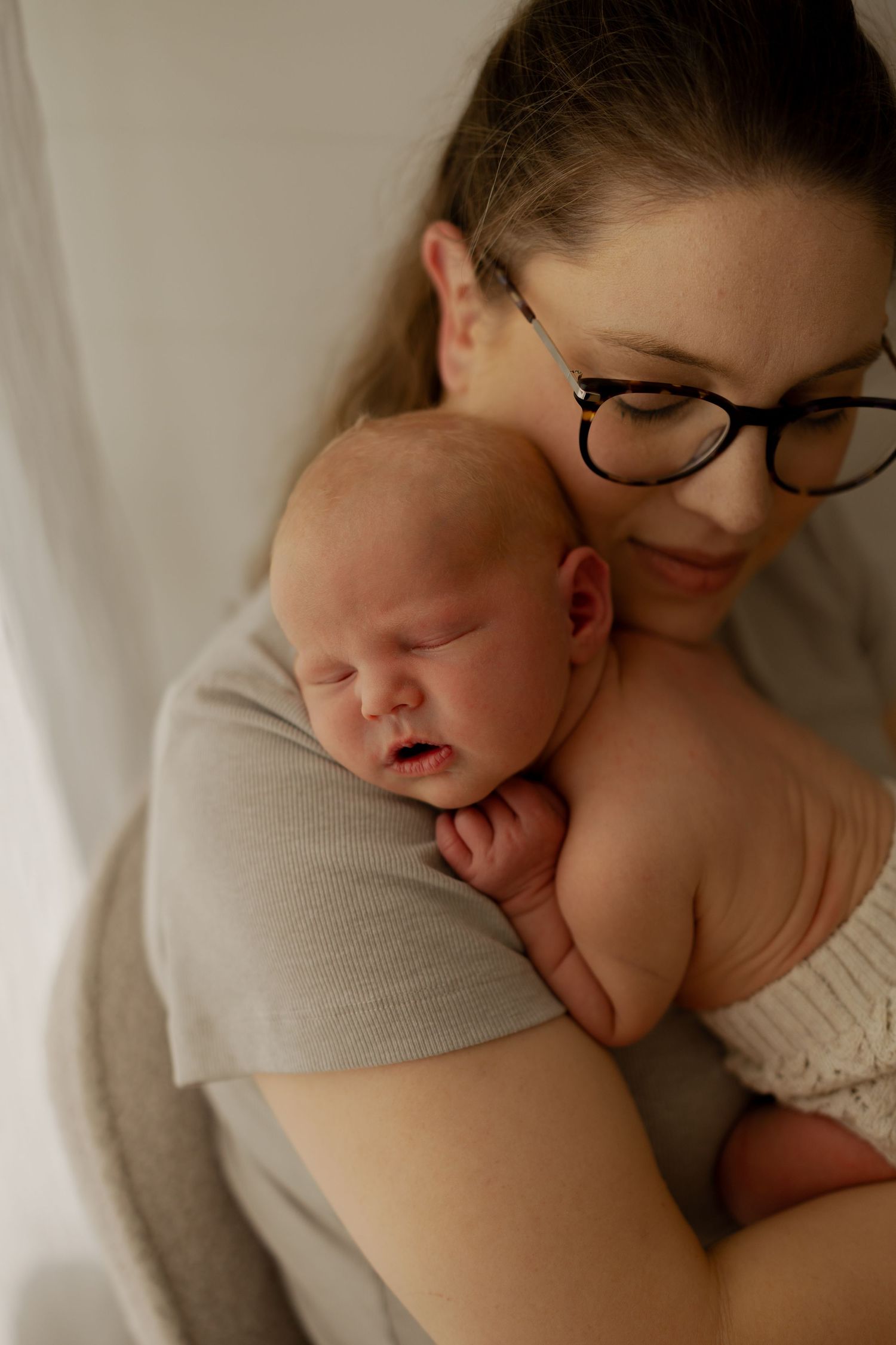 A tender moment showing a sleeping baby nestled against someone in soft, natural lighting.