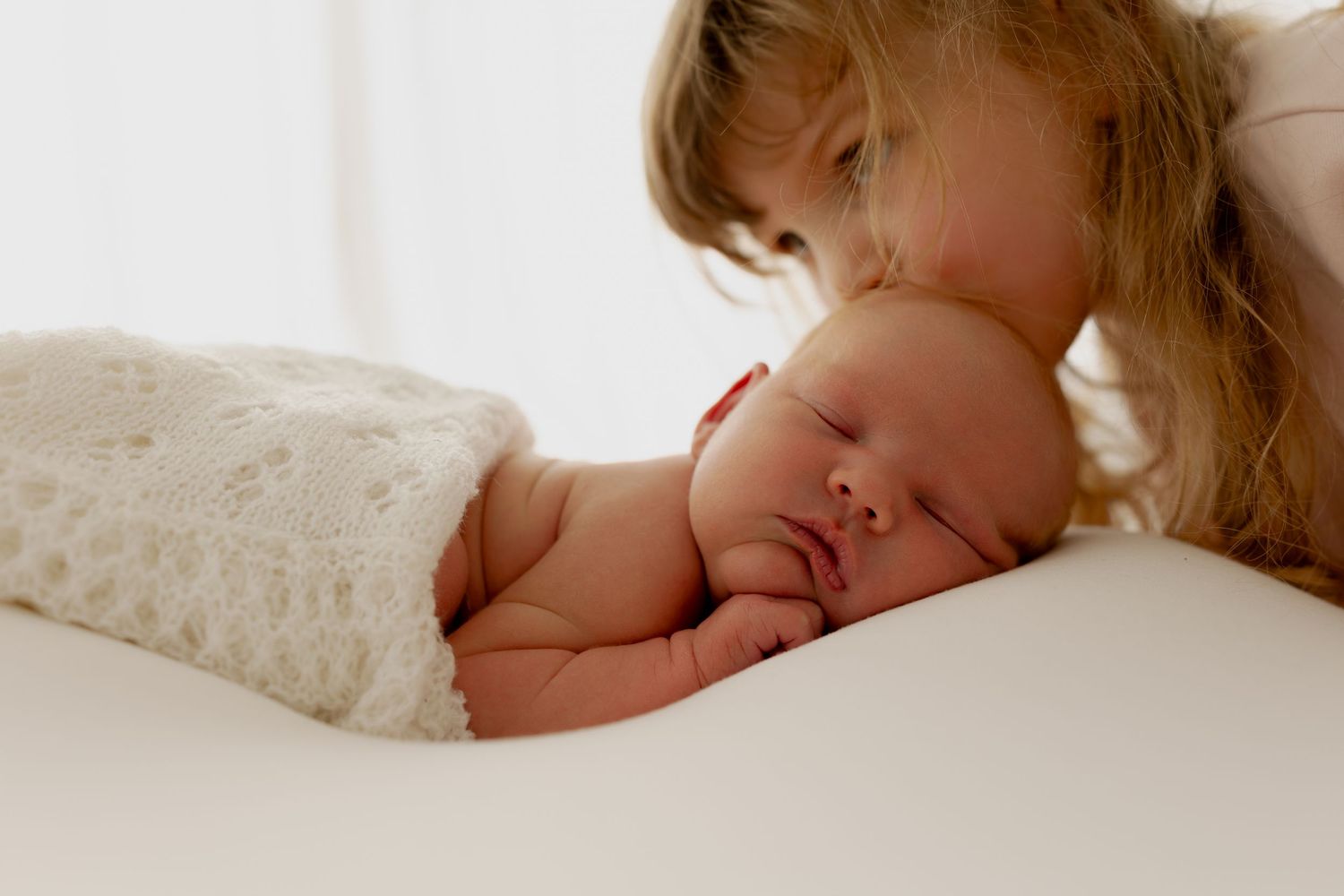 A sleeping newborn baby rests peacefully under a soft white blanket while being gently embraced.