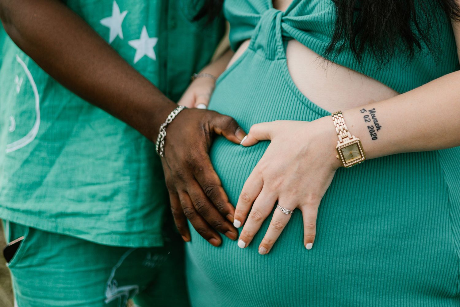 Two hands wearing silver jewelry forming a heart shape against turquoise clothing.