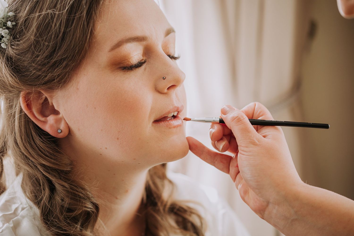 Close up of makeup artist applying lipstick on bride during wedding preparation.