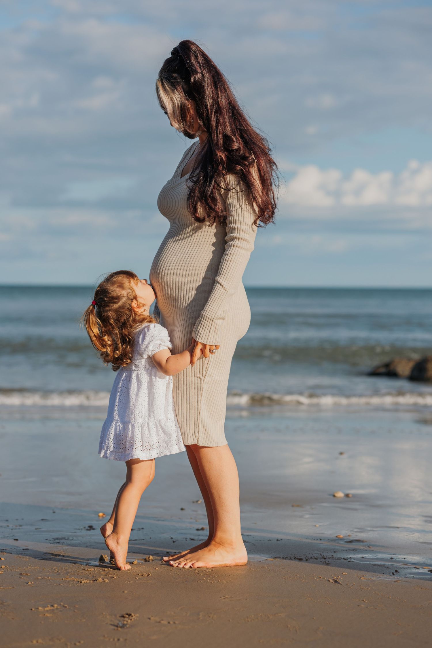 Mother and young daughter share special moment on beach as waves roll in background.