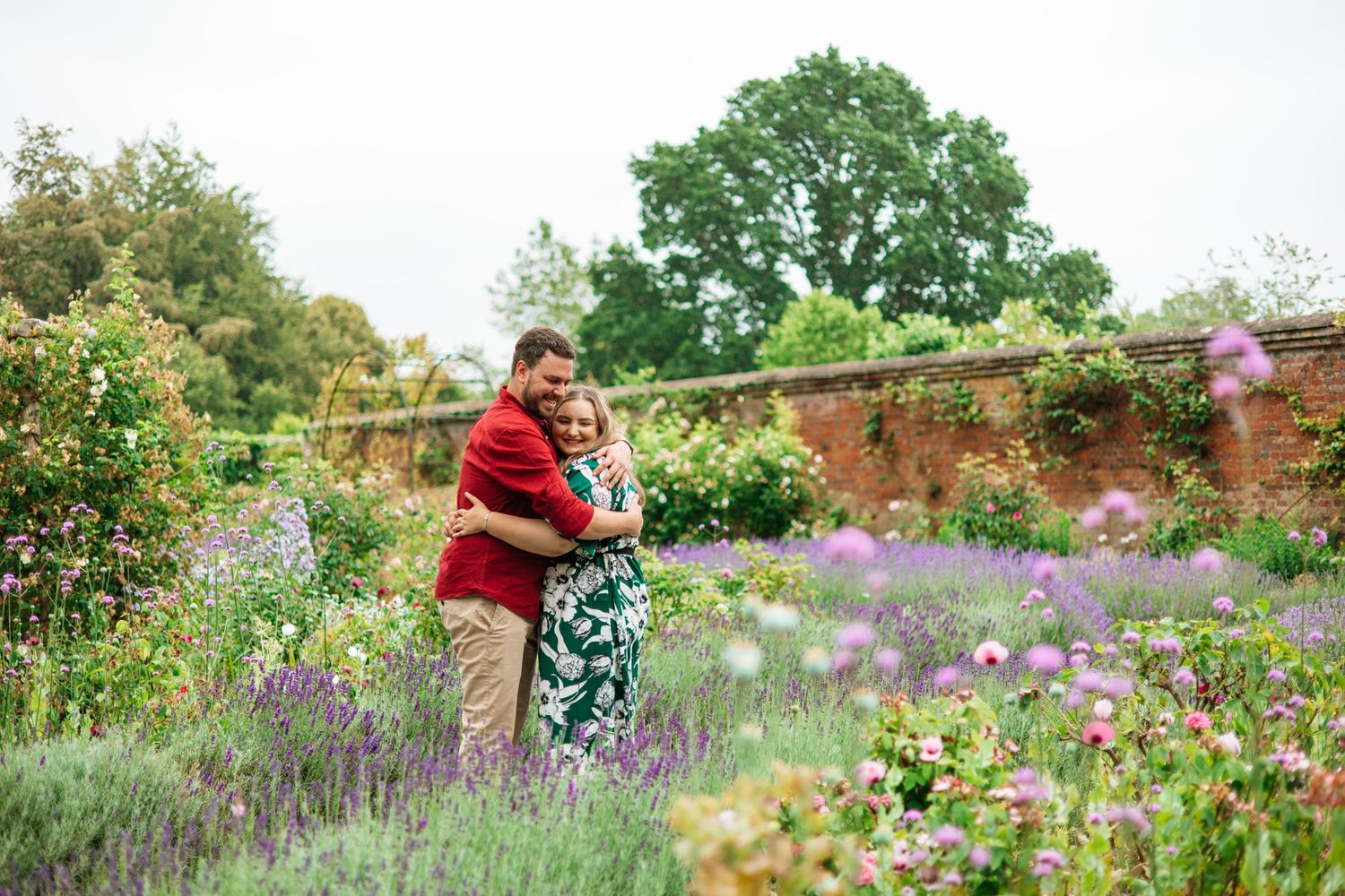 A couple embraces in a vibrant garden filled with purple flowers and greenery.