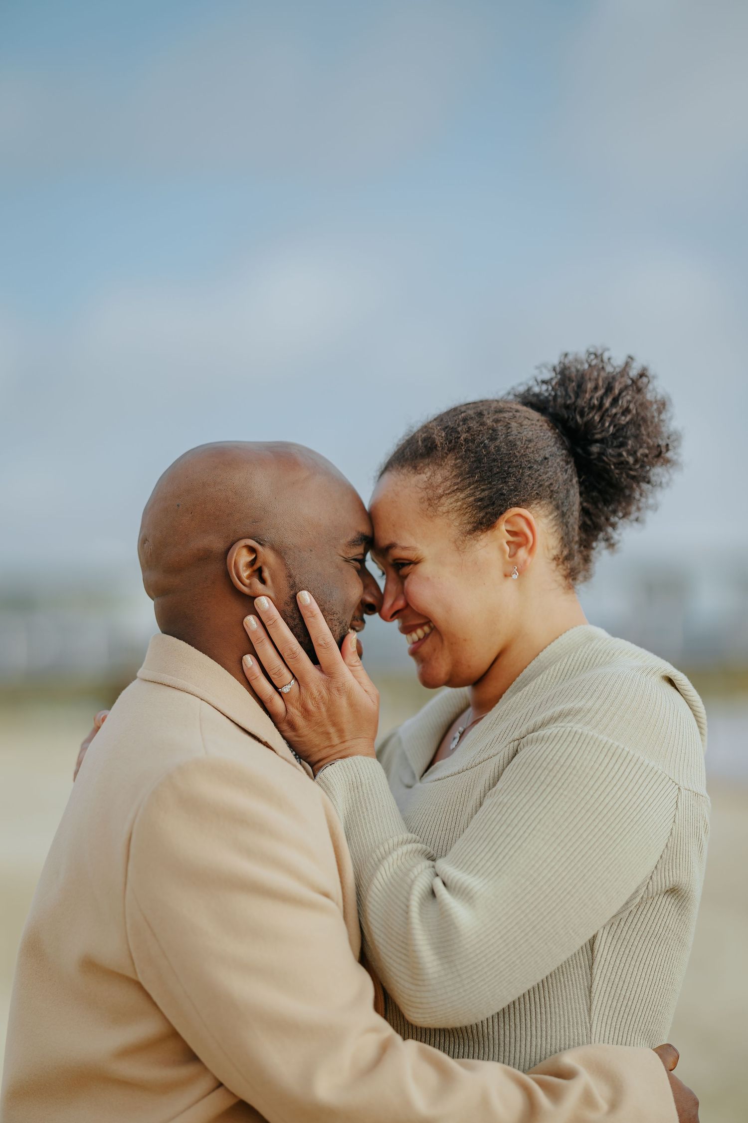 A couple in warm sweaters share an intimate moment outdoors with their foreheads touching in tender affection.