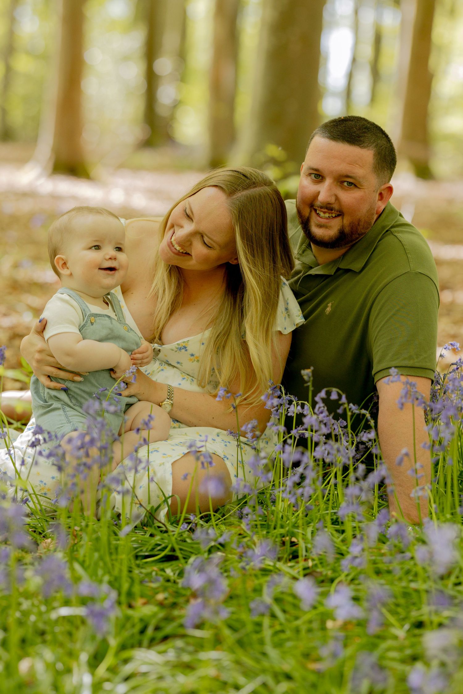 Family enjoying playful moment together in purple bluebell woodland setting.