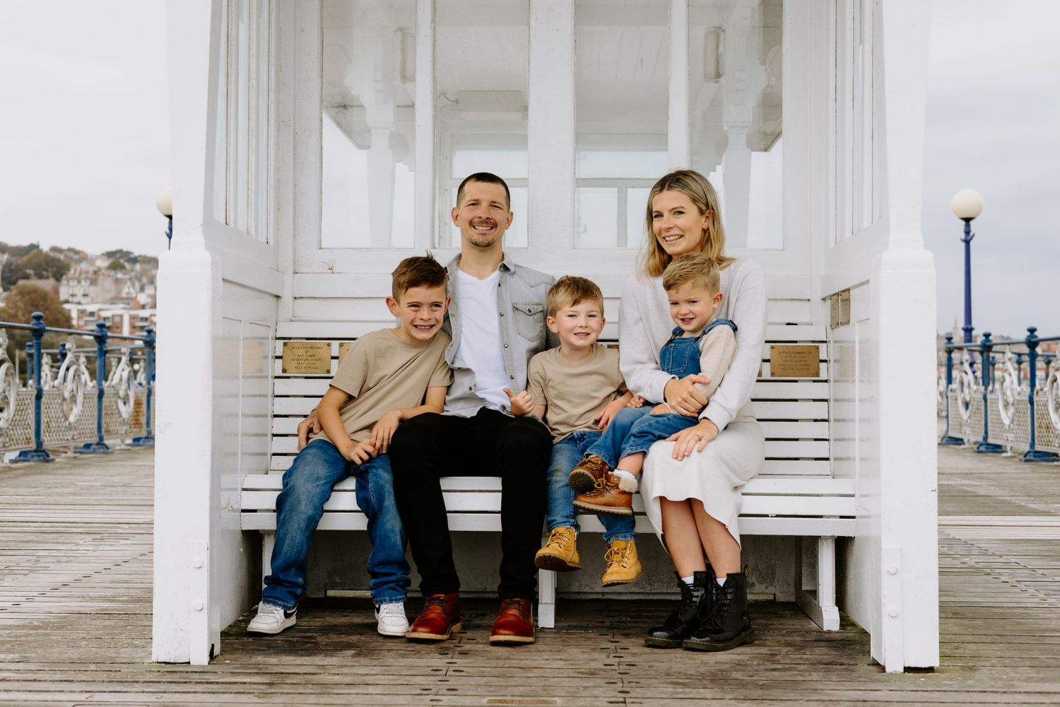 Family sitting together on white wooden bench on seaside pier.