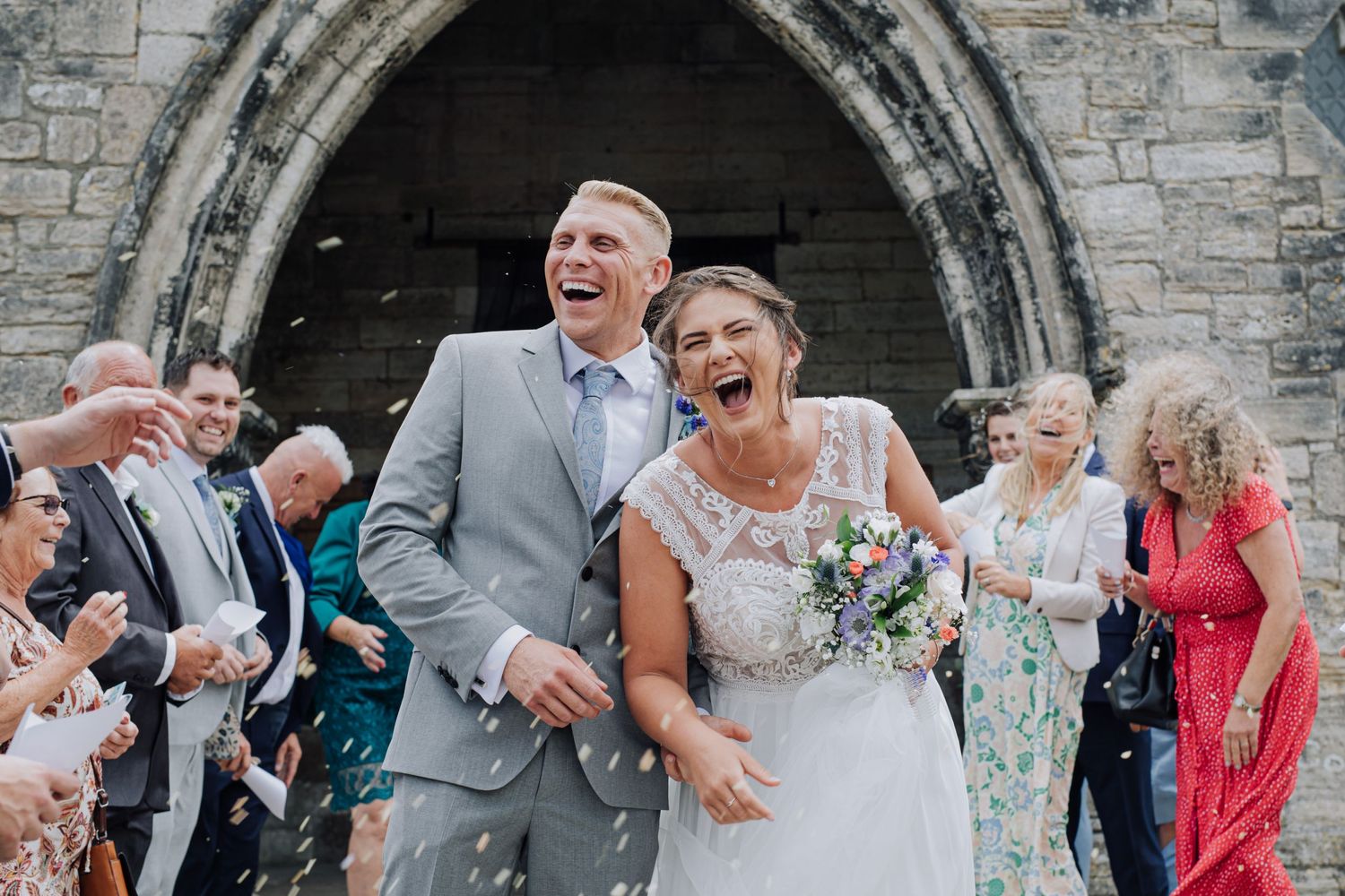 Wedding party celebrates with joy outside a stone church archway.