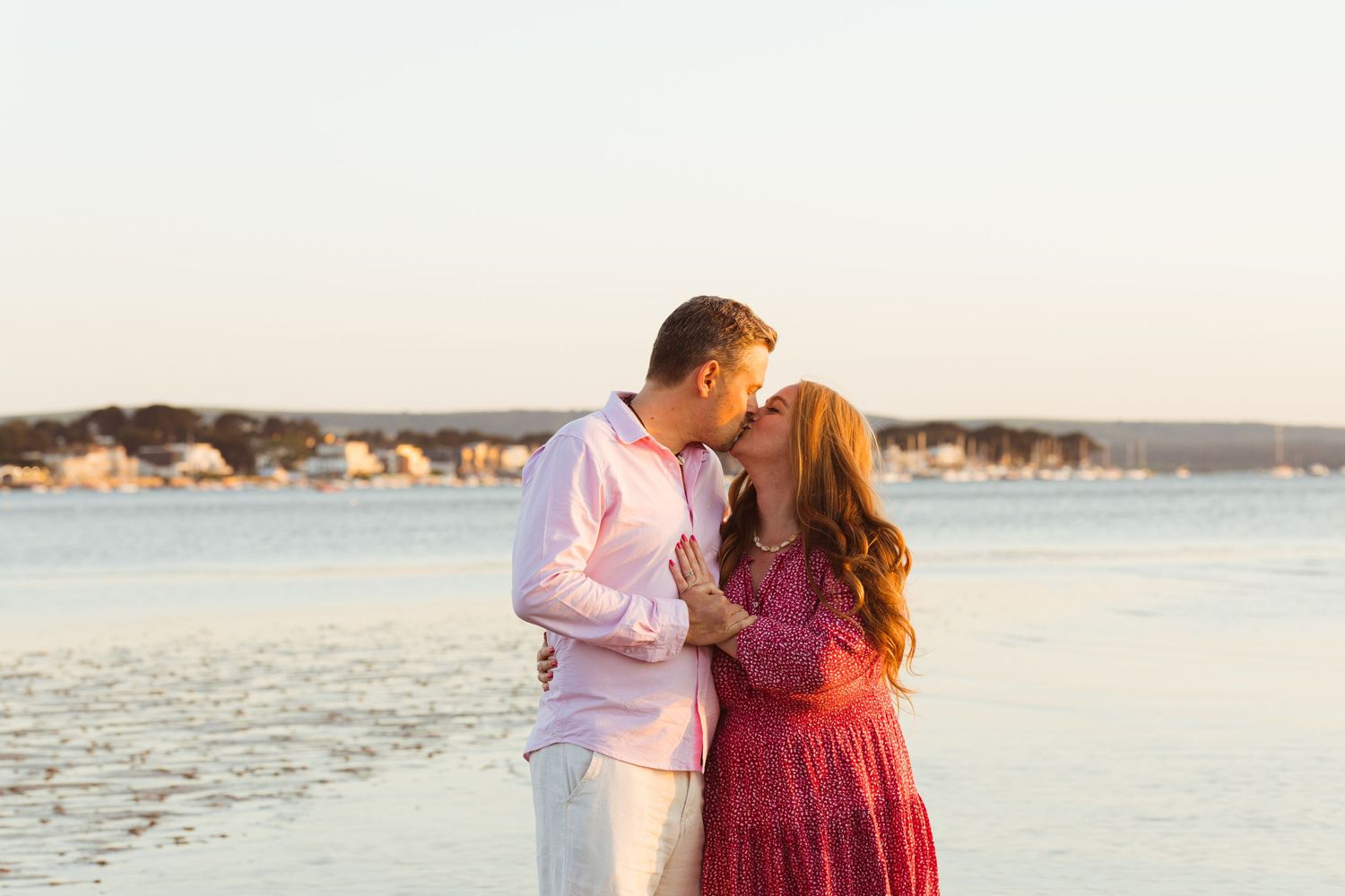 Happy couple in coordinated outfits share loving moment by waterfront at sunset.