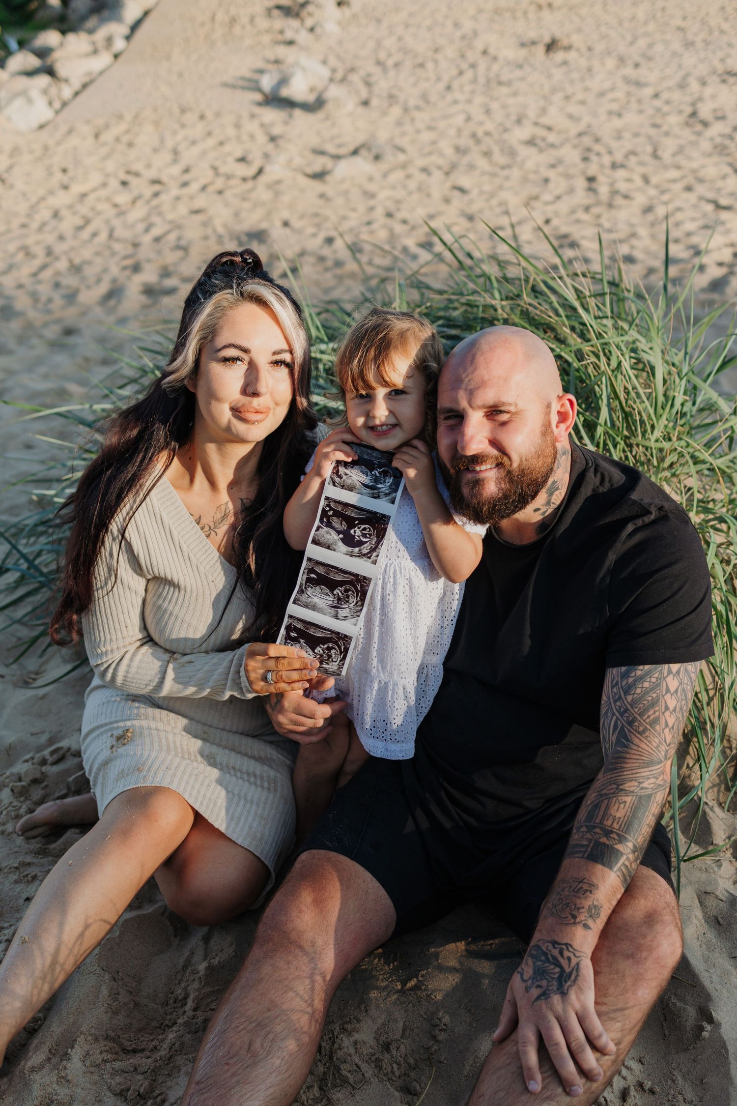 Family sitting on beach dunes sharing ultrasound photos together.