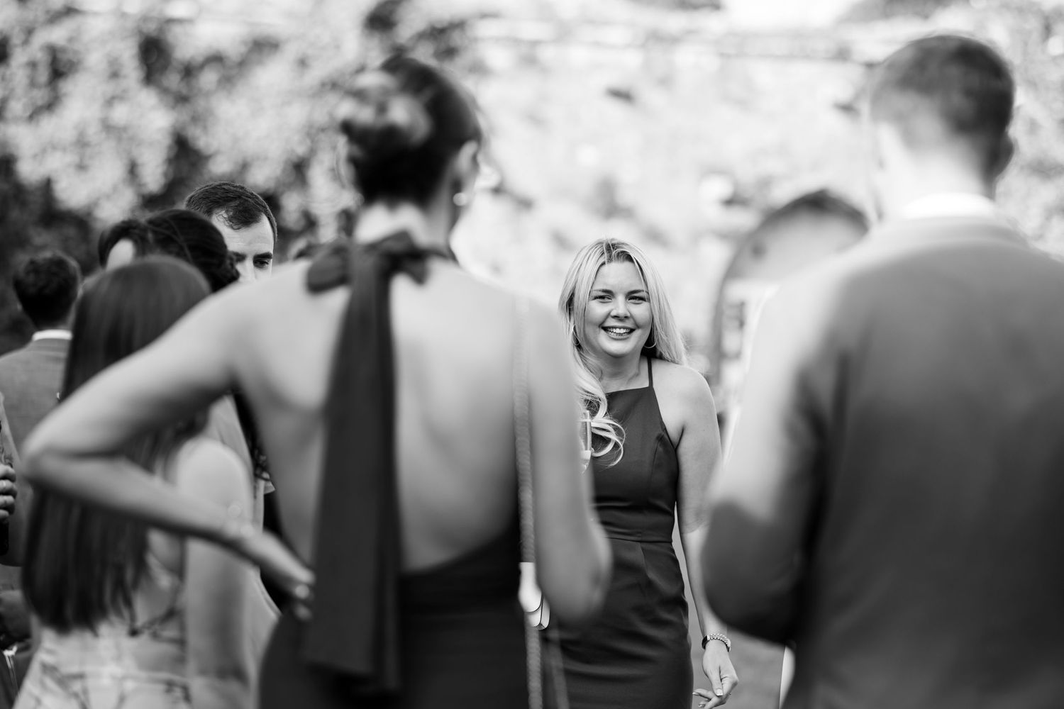 A candid black and white photo of guests mingling at an outdoor social gathering.