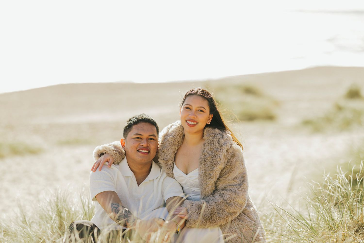 Couple sharing a joyful moment together on a sunny beach with sand dunes in background.