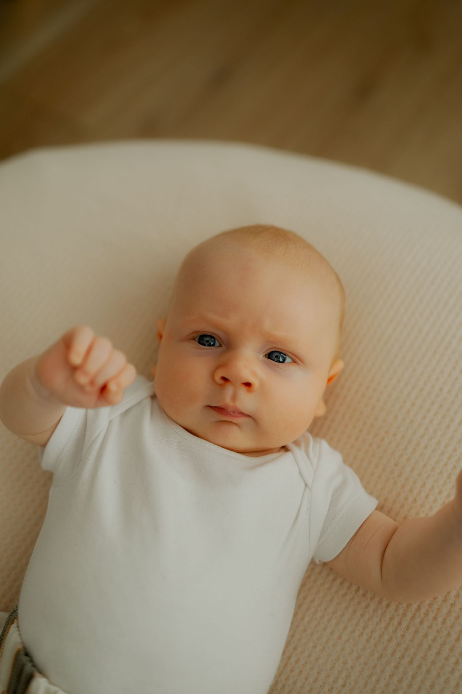 A baby wearing white clothing lies on a white textured surface in a series of connected photos.