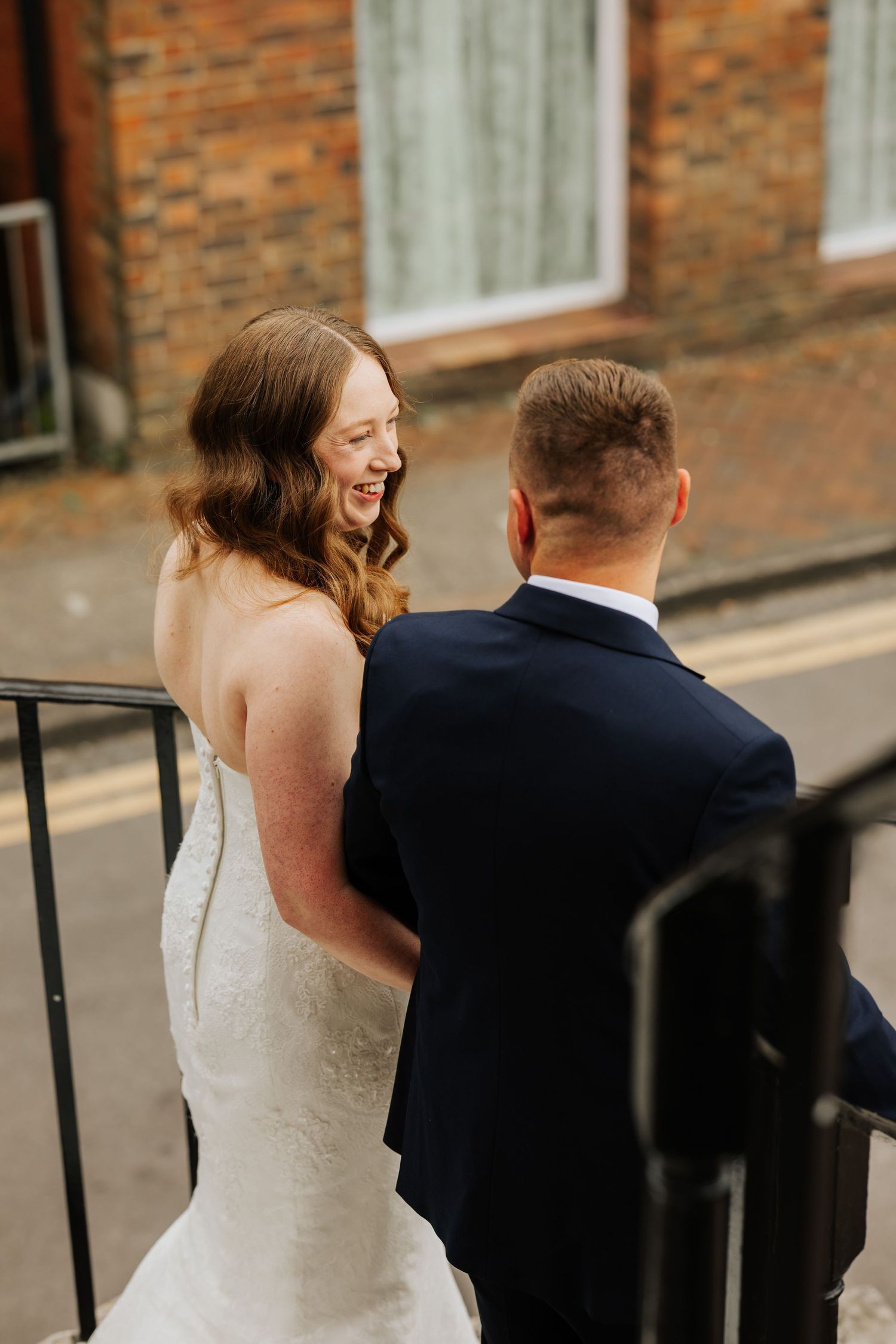 A joyful couple share a laugh together on an outdoor staircase during their wedding day.