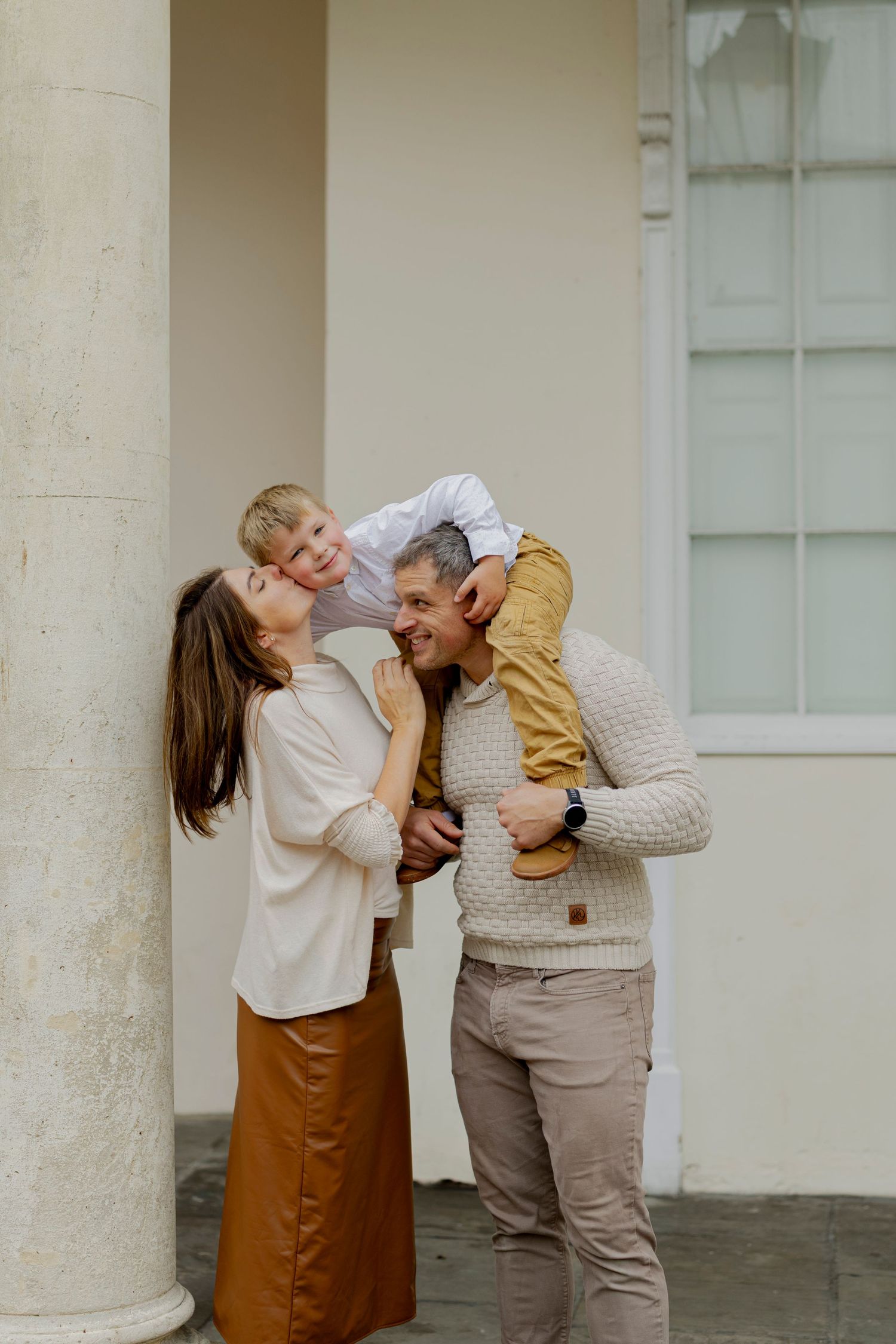 Happy family with young child on father's shoulders sharing a joyful moment outside a classic building.