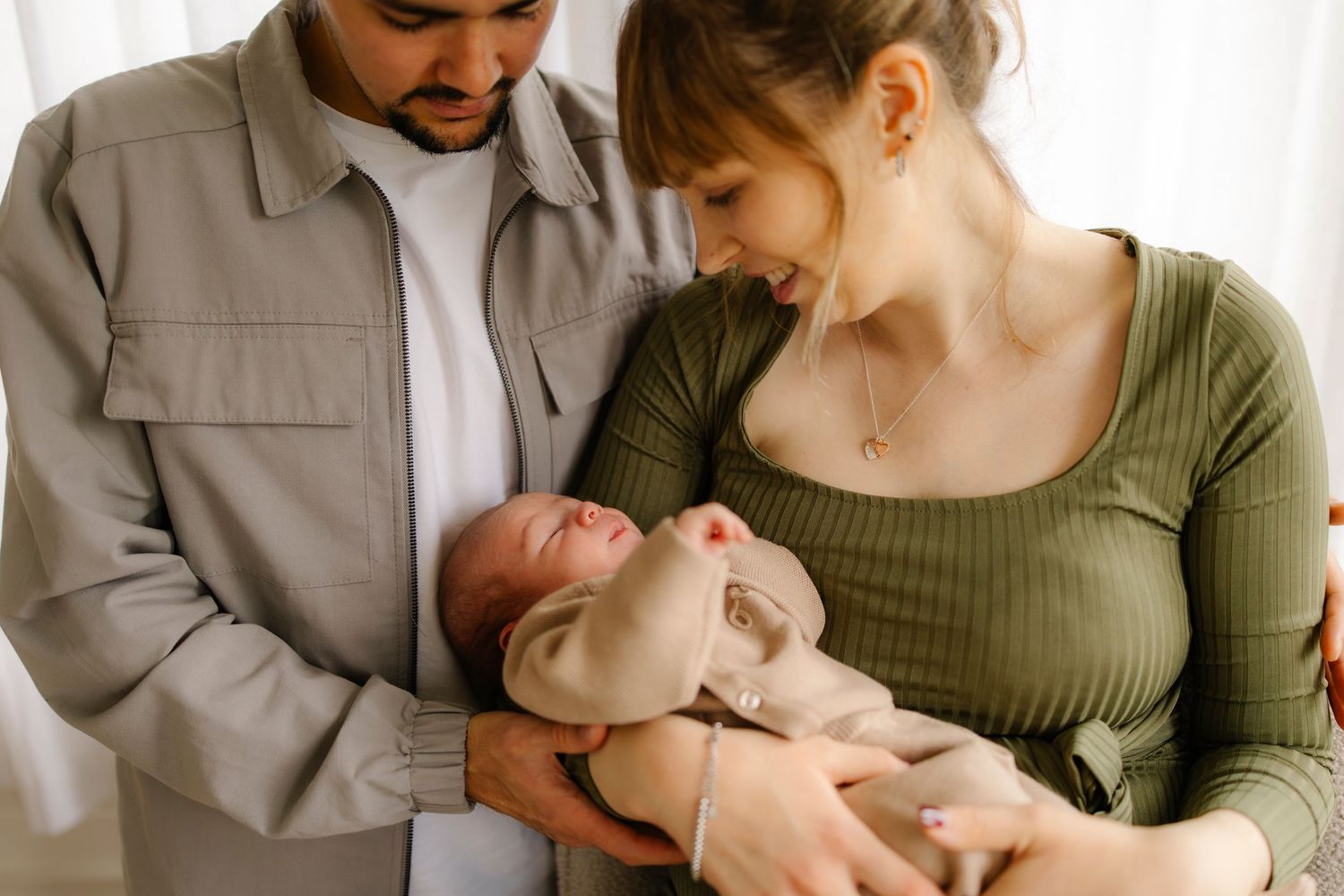 Parents in neutral and olive green clothing share tender moments with their newborn baby in a series of connected photos.