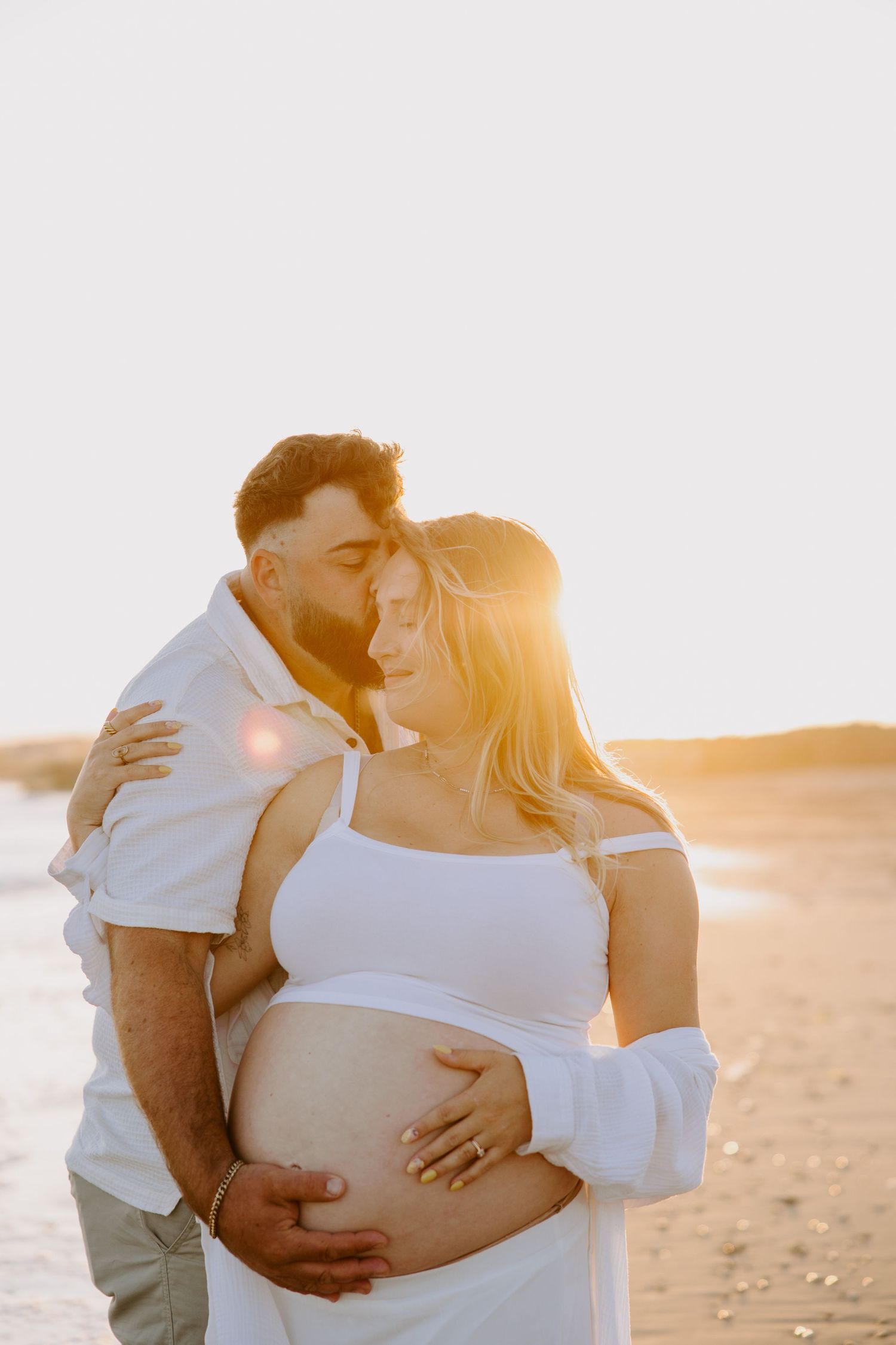 Romantic sunset maternity photo of couple embracing on beach.