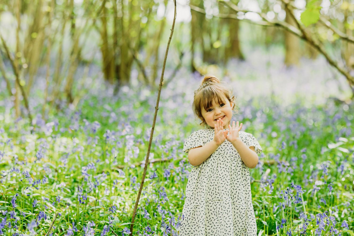 Child in polka dot dress poses playfully among blooming bluebells.