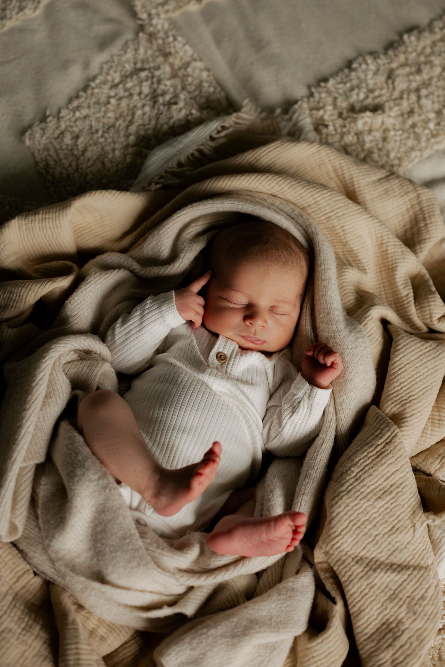 A sleeping newborn baby wrapped in cozy beige knit blankets on soft textured bedding.