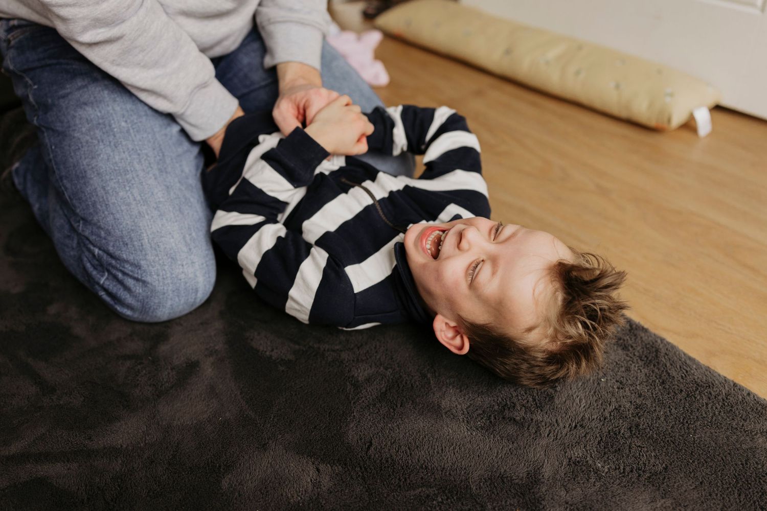 Child lying on dark carpet wearing striped clothing while playing and laughing.