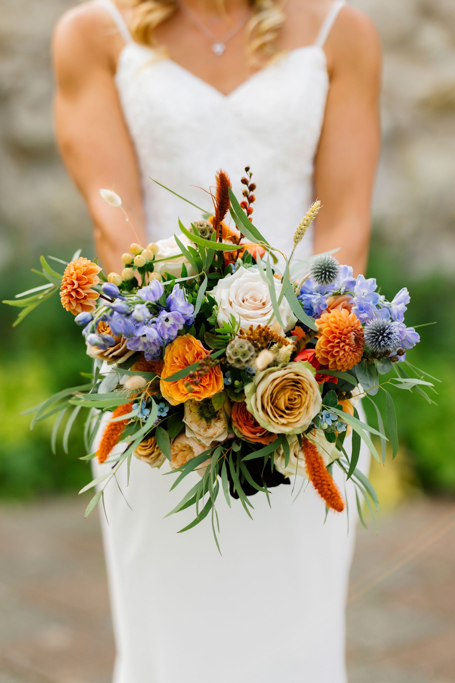 A vibrant bridal bouquet featuring orange, purple, and cream flowers with natural greenery.