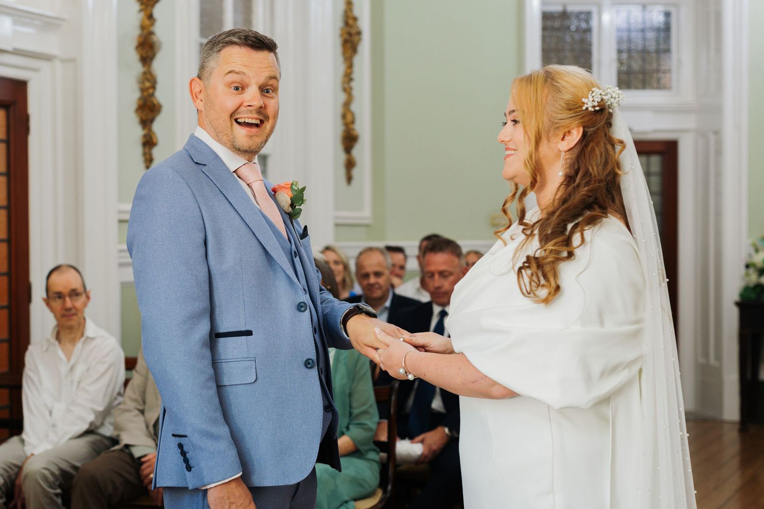 Wedding ceremony taking place in an elegant white room with ornate decor.