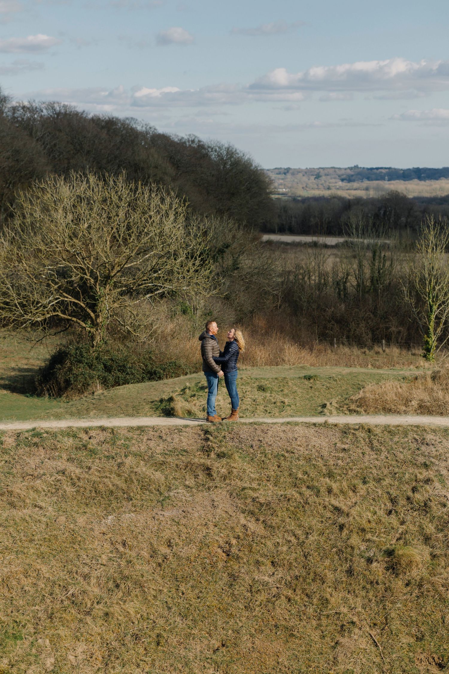 Couple standing together on hilltop path with scenic countryside view.