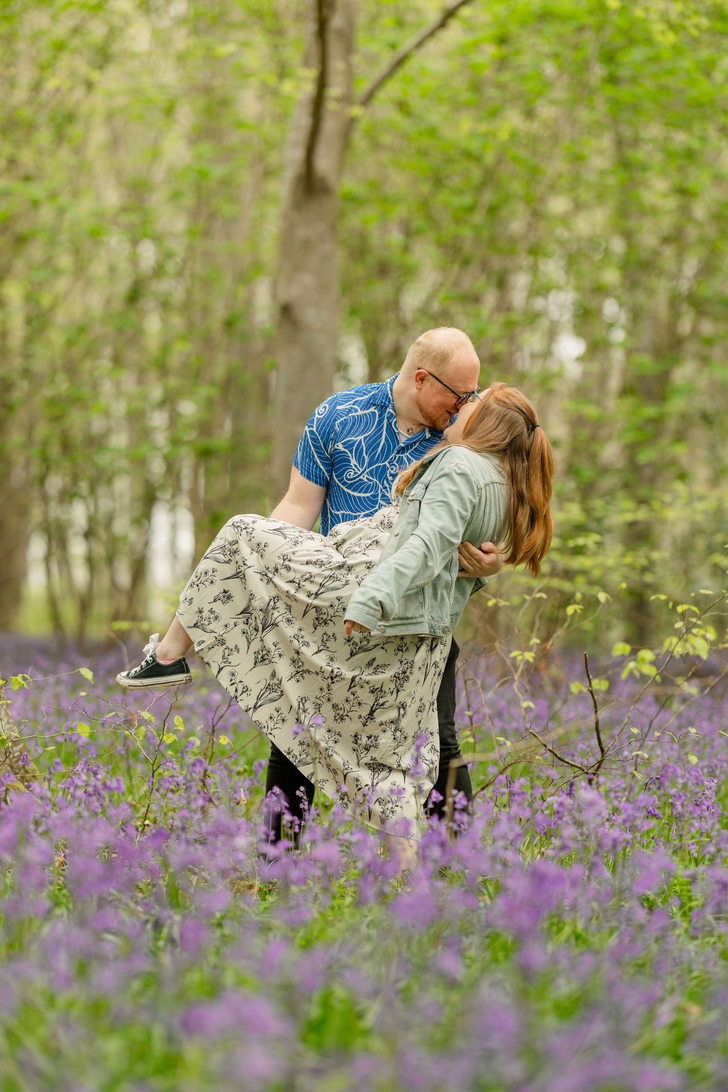 A romantic couple dances together in a dreamy spring forest filled with blooming purple wildflowers.