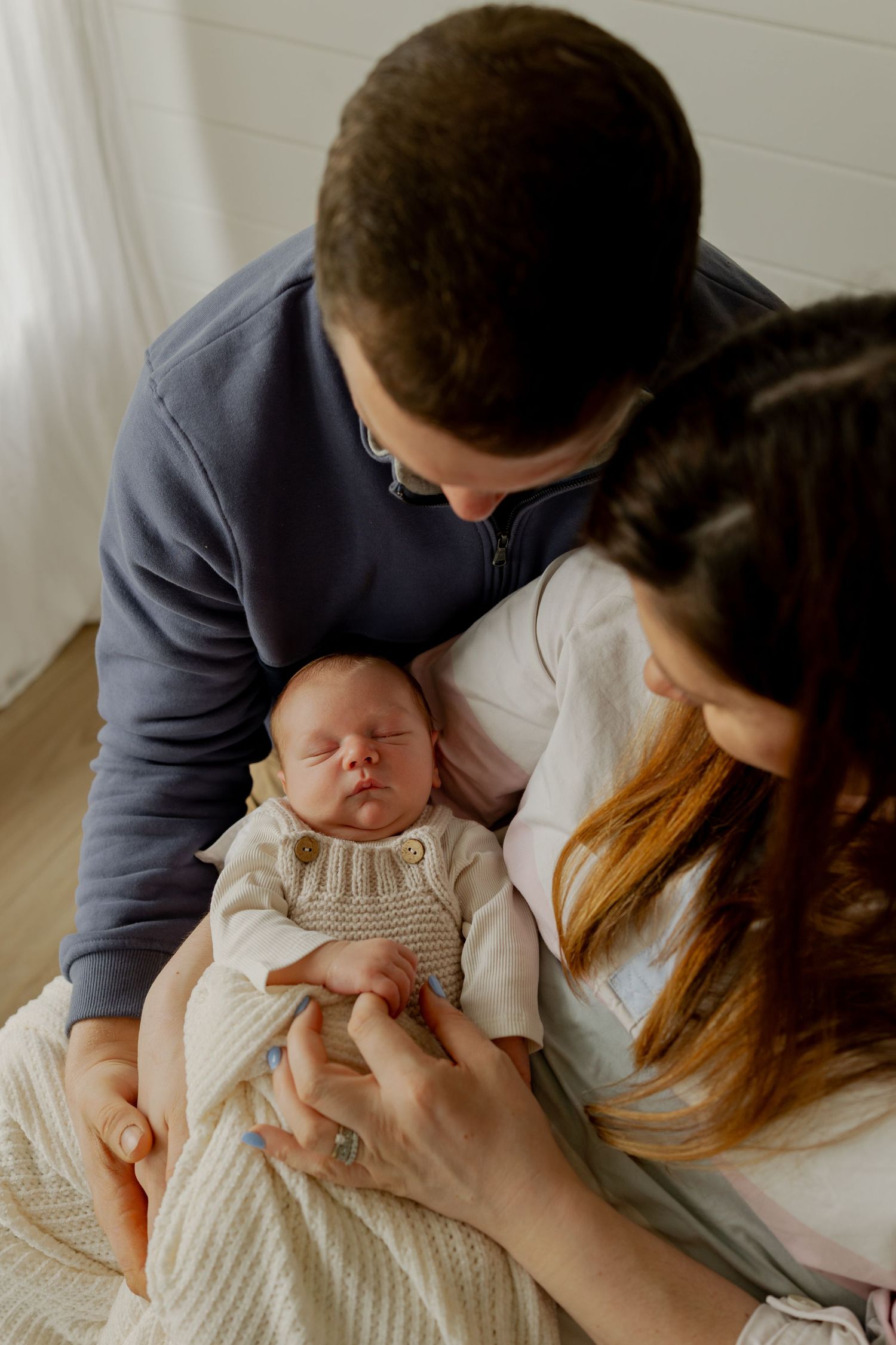 New parents lovingly gaze at their sleeping newborn baby wrapped in a cozy knit blanket.