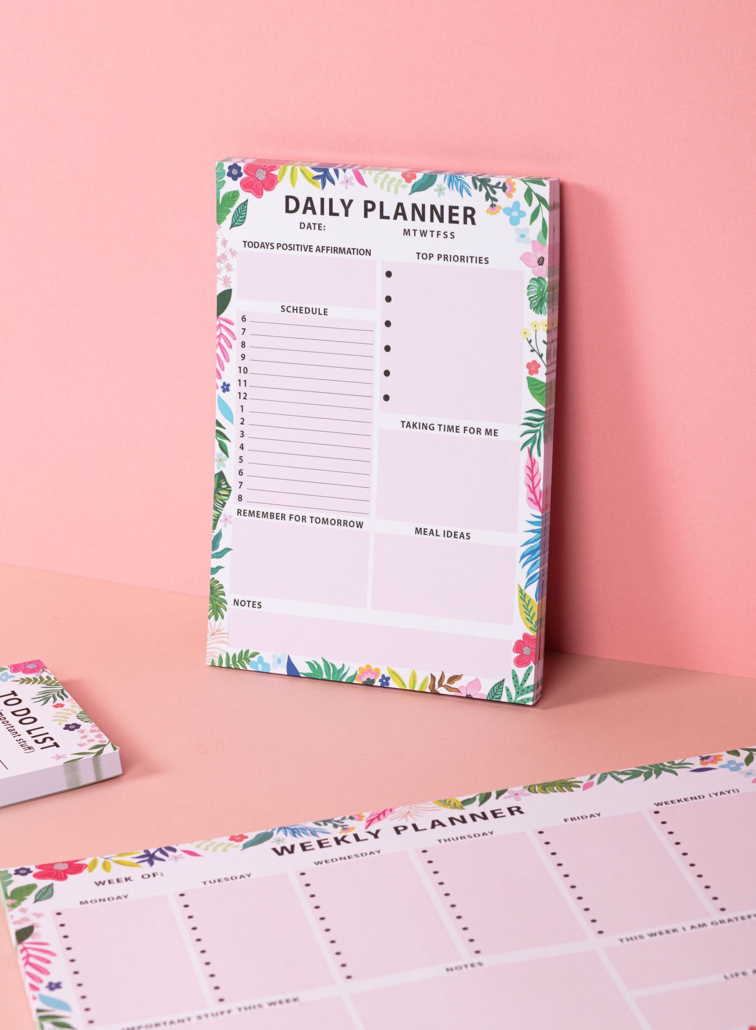 Floral-bordered daily and weekly planner pages with task lists against a pink background.