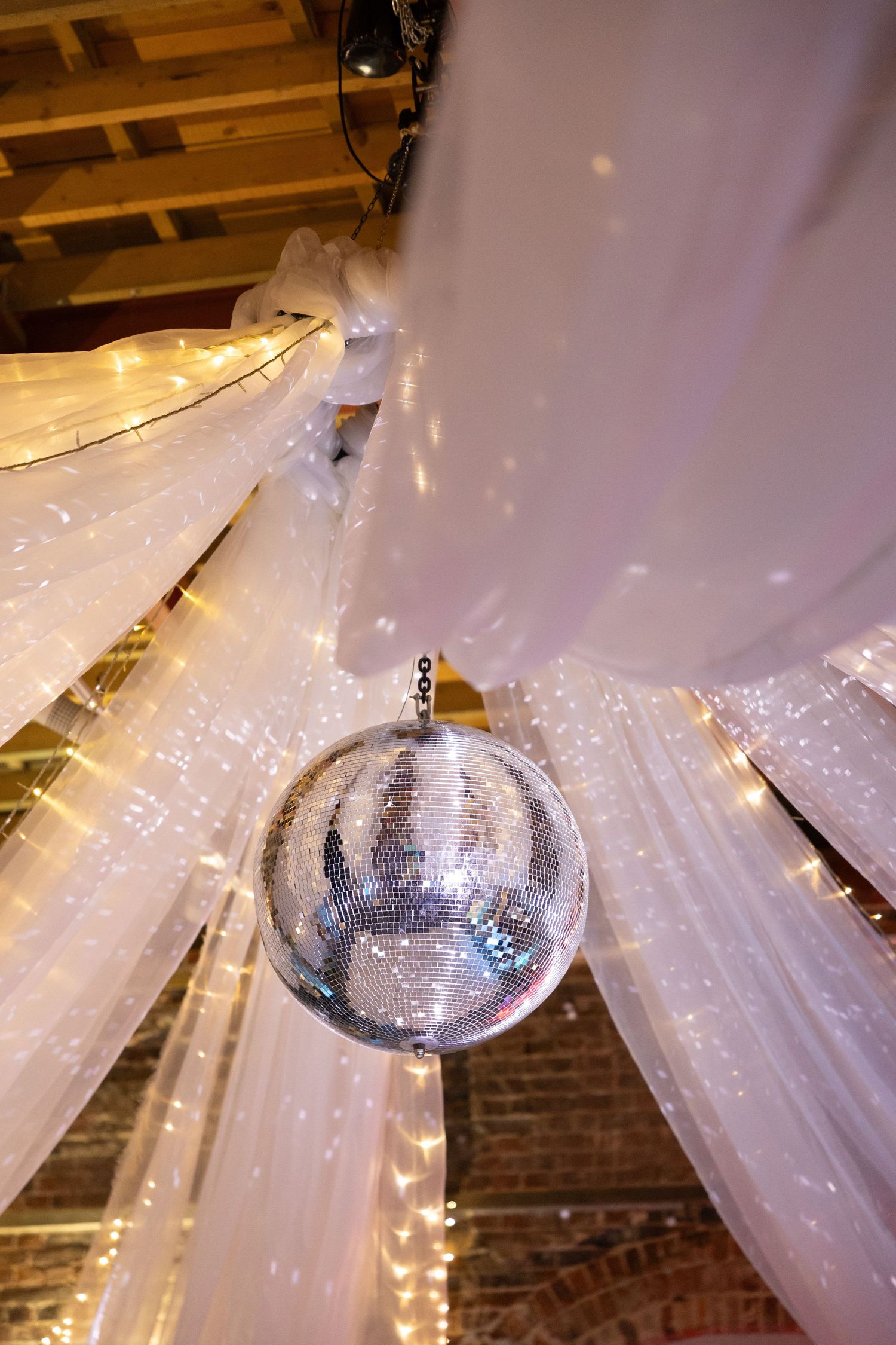 A disco ball hangs from draped white fabric with twinkling lights creating a magical atmosphere.