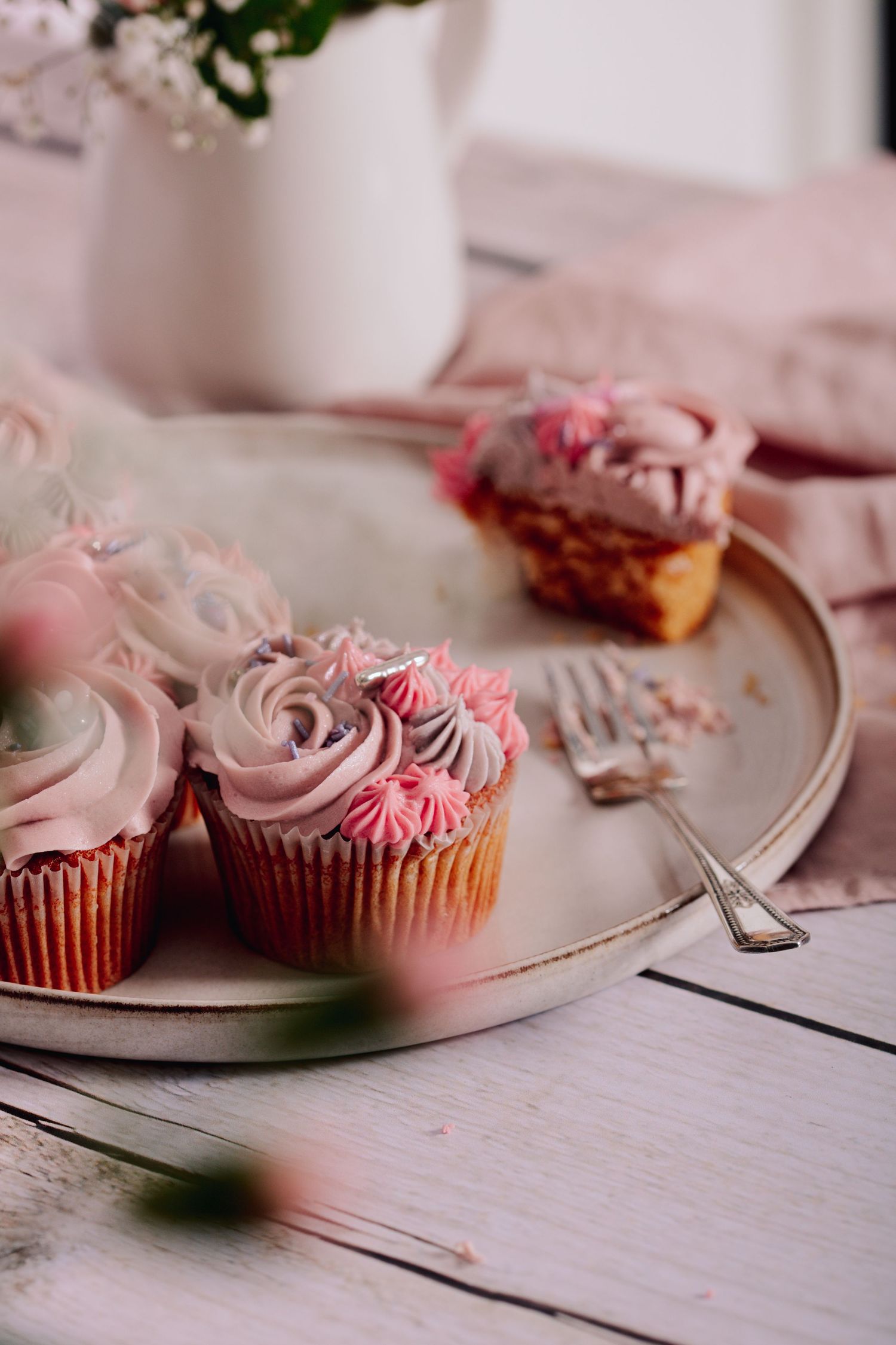 Pink frosted cupcakes with rosette swirl decorations on a vintage plate with delicate floral details.