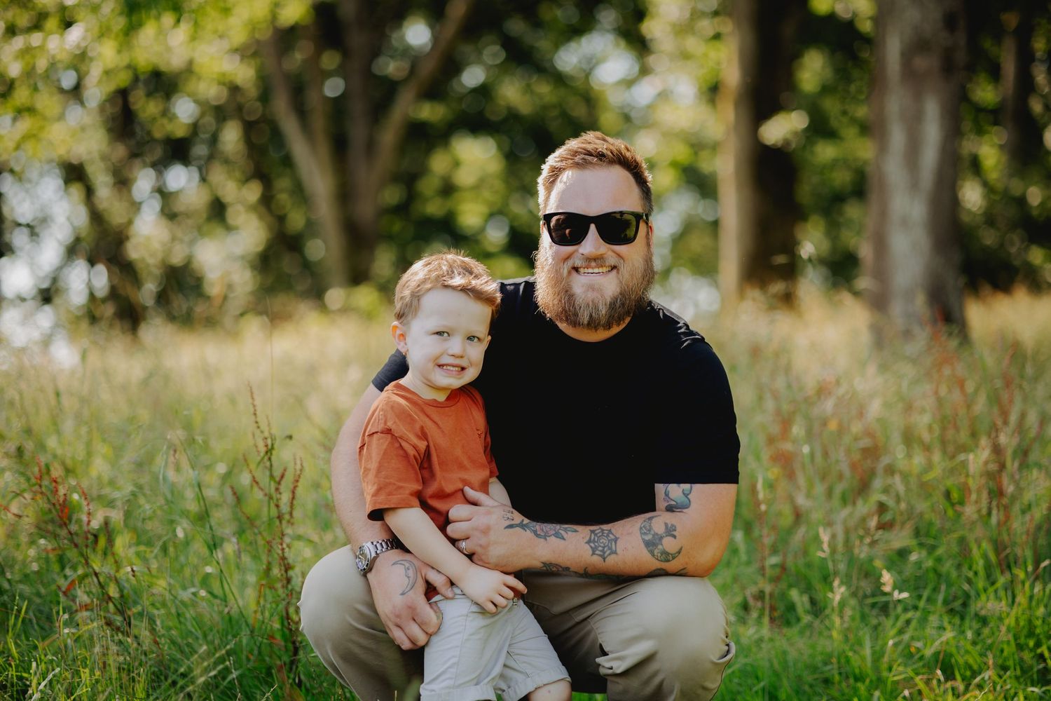 Parent and young child posing together in a grassy outdoor setting during golden hour.