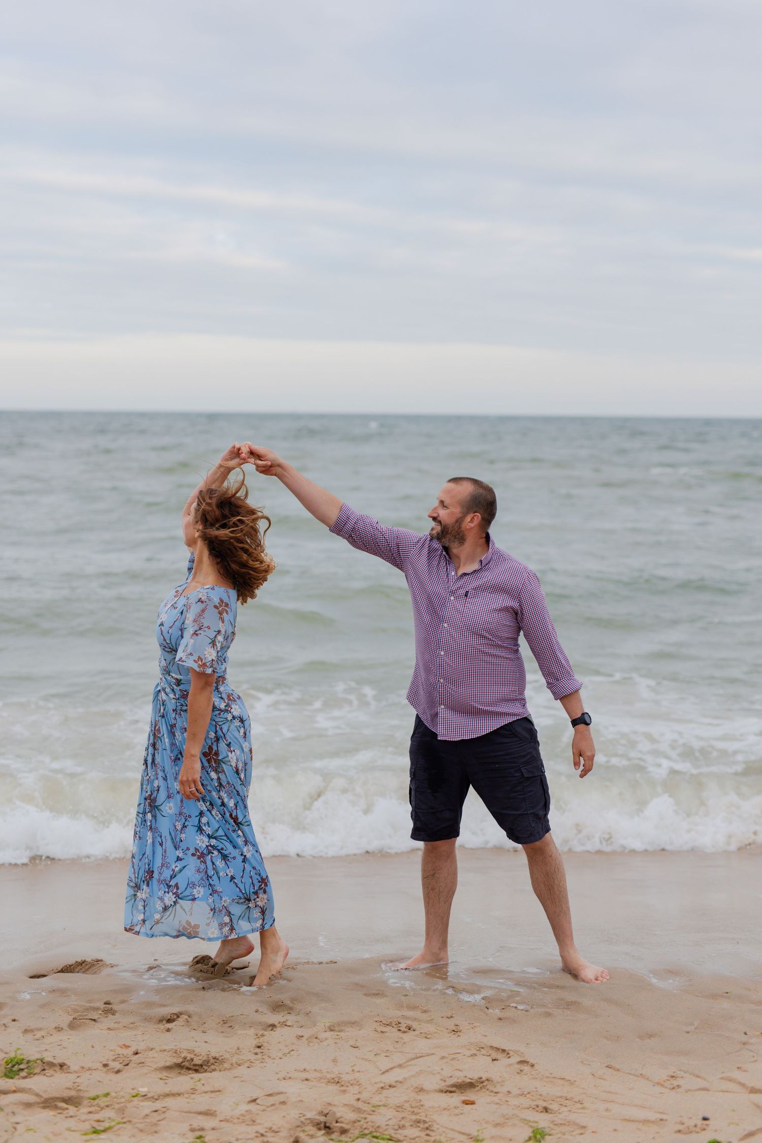 A couple dances together on the beach with waves crashing behind them.