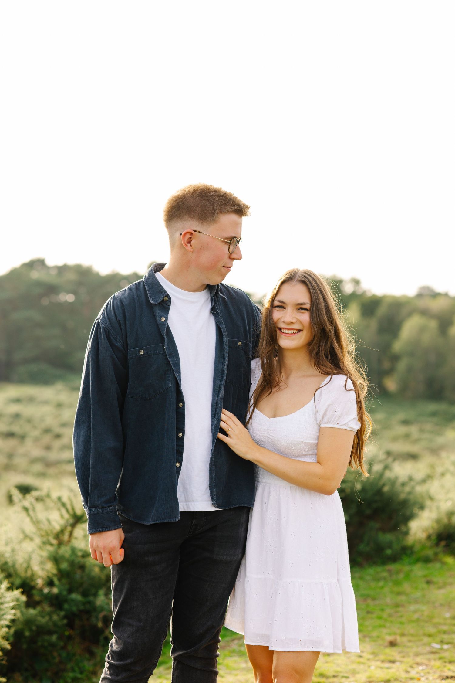 A couple poses together on a green hillside during a romantic outdoor photoshoot.