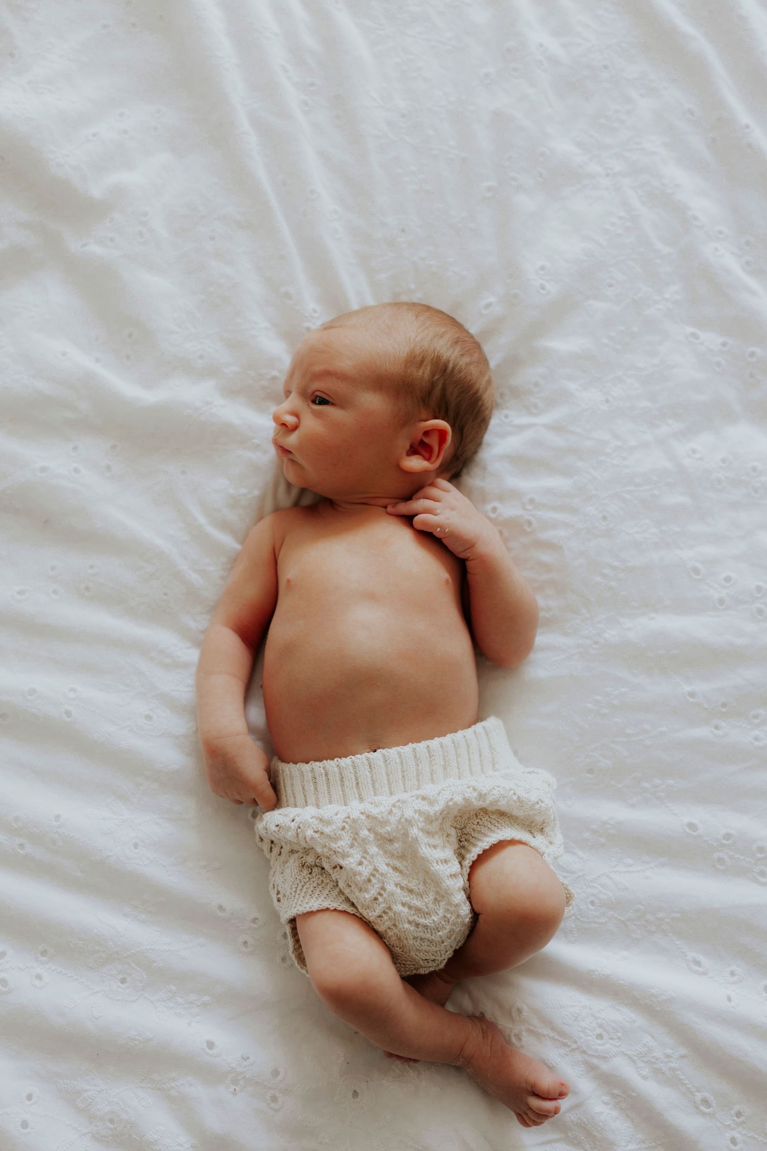 Peaceful newborn baby laying on white sheets wearing a knitted diaper cover.