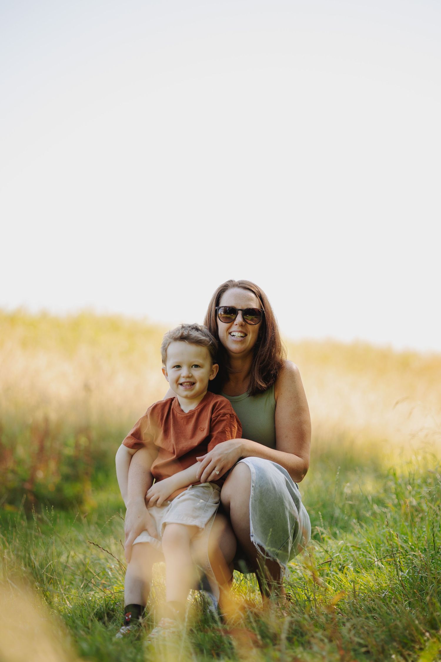 Family portrait of mother and child sitting together in a sunny field with wildflowers.
