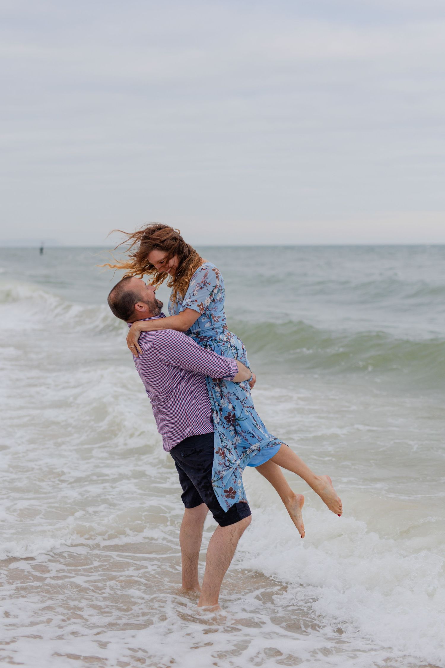 A couple plays in the ocean waves during a beach photoshoot.
