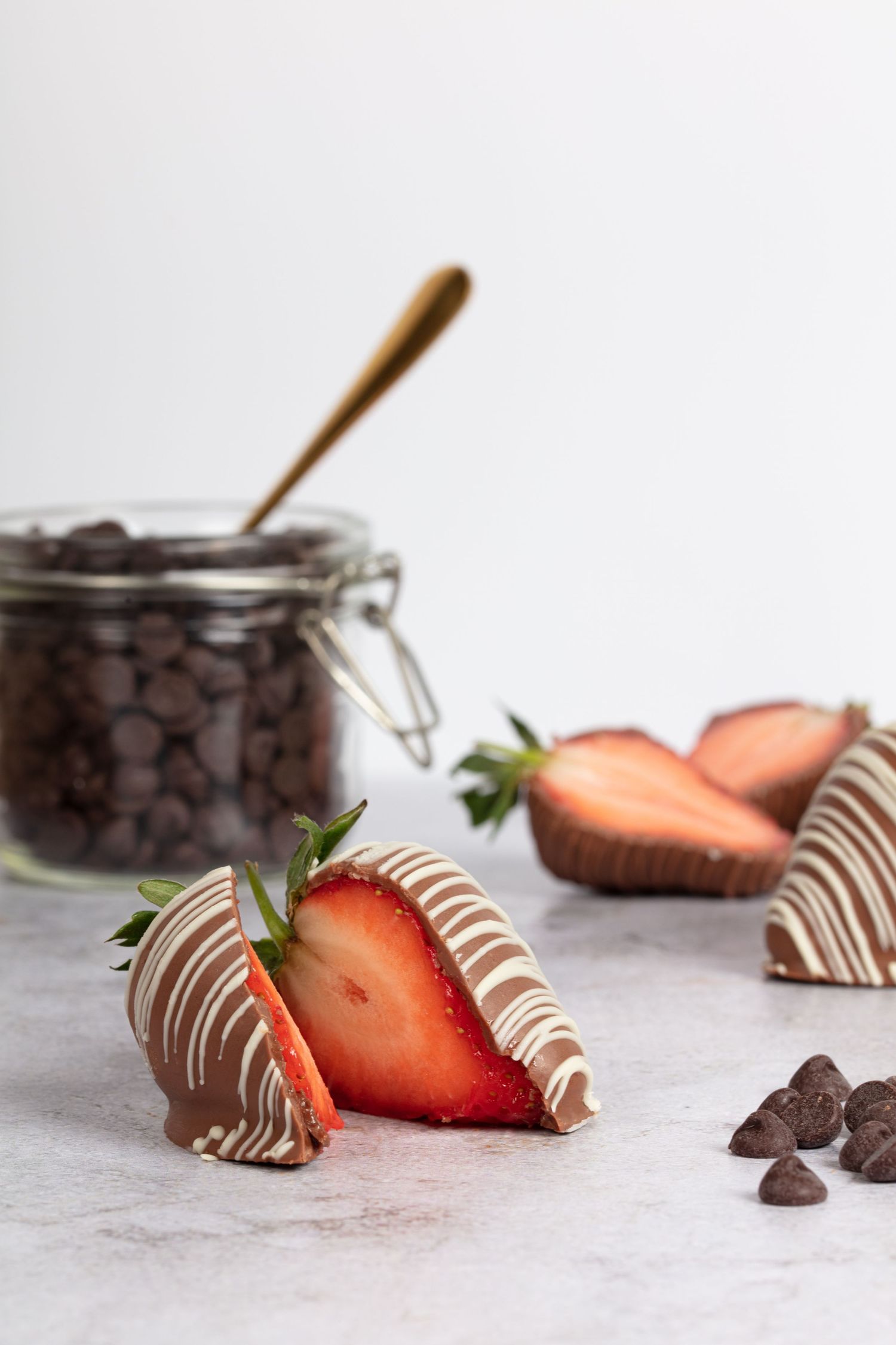 Fresh strawberries drizzled with white chocolate alongside chocolate chips and a jar of dark chocolate pieces.