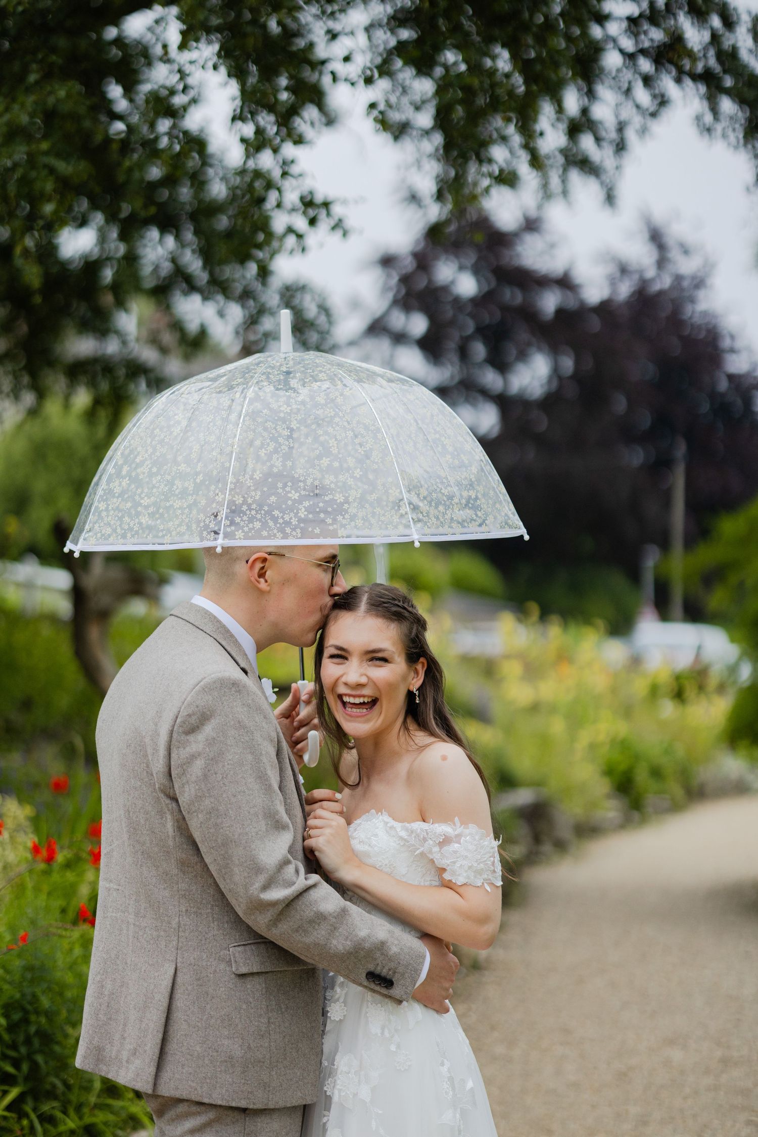 Couple sharing a joyful moment under a clear umbrella in a garden setting.