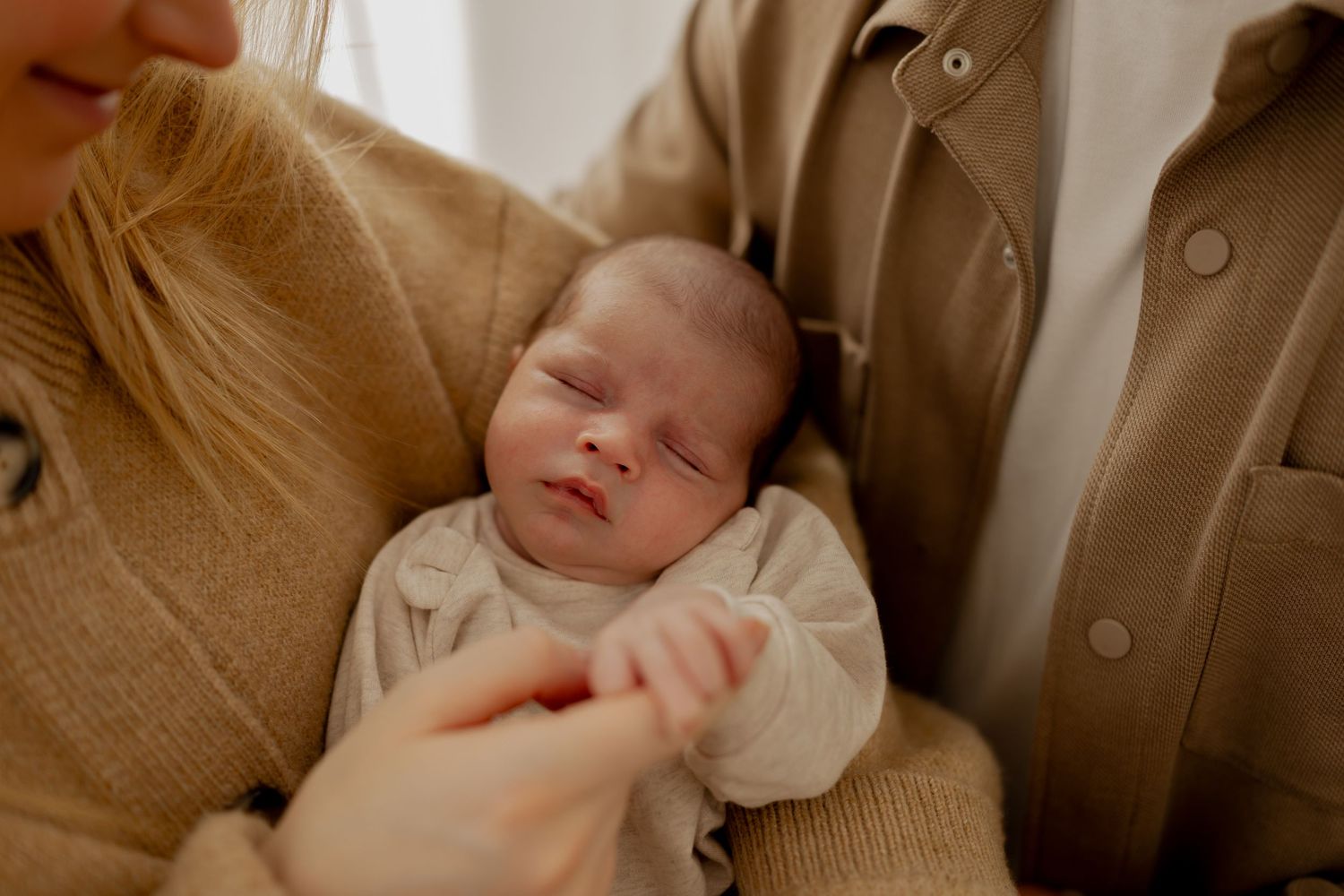 A sleeping baby nestled in a cozy beige blanket rests peacefully in a warm, natural light setting.