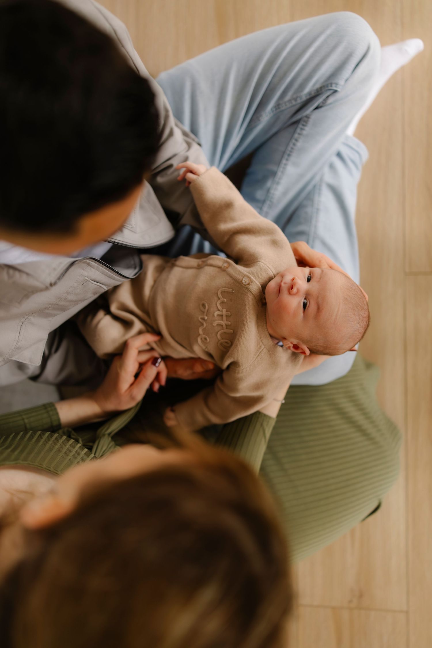 Tender moment of a baby lying on a green mat while being gently touched by someone's hand.
