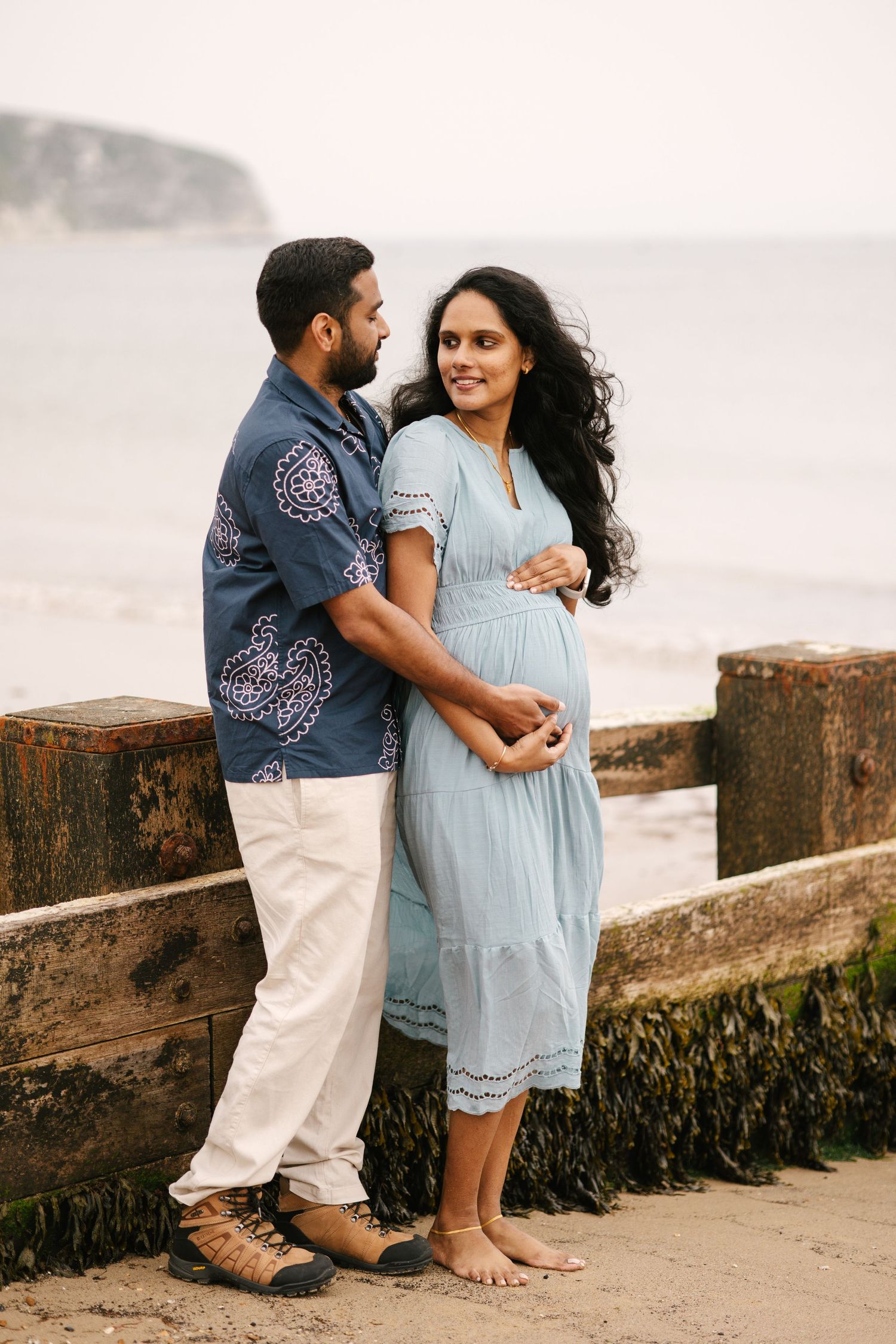 Expecting couple sharing intimate moment on coastal boardwalk.