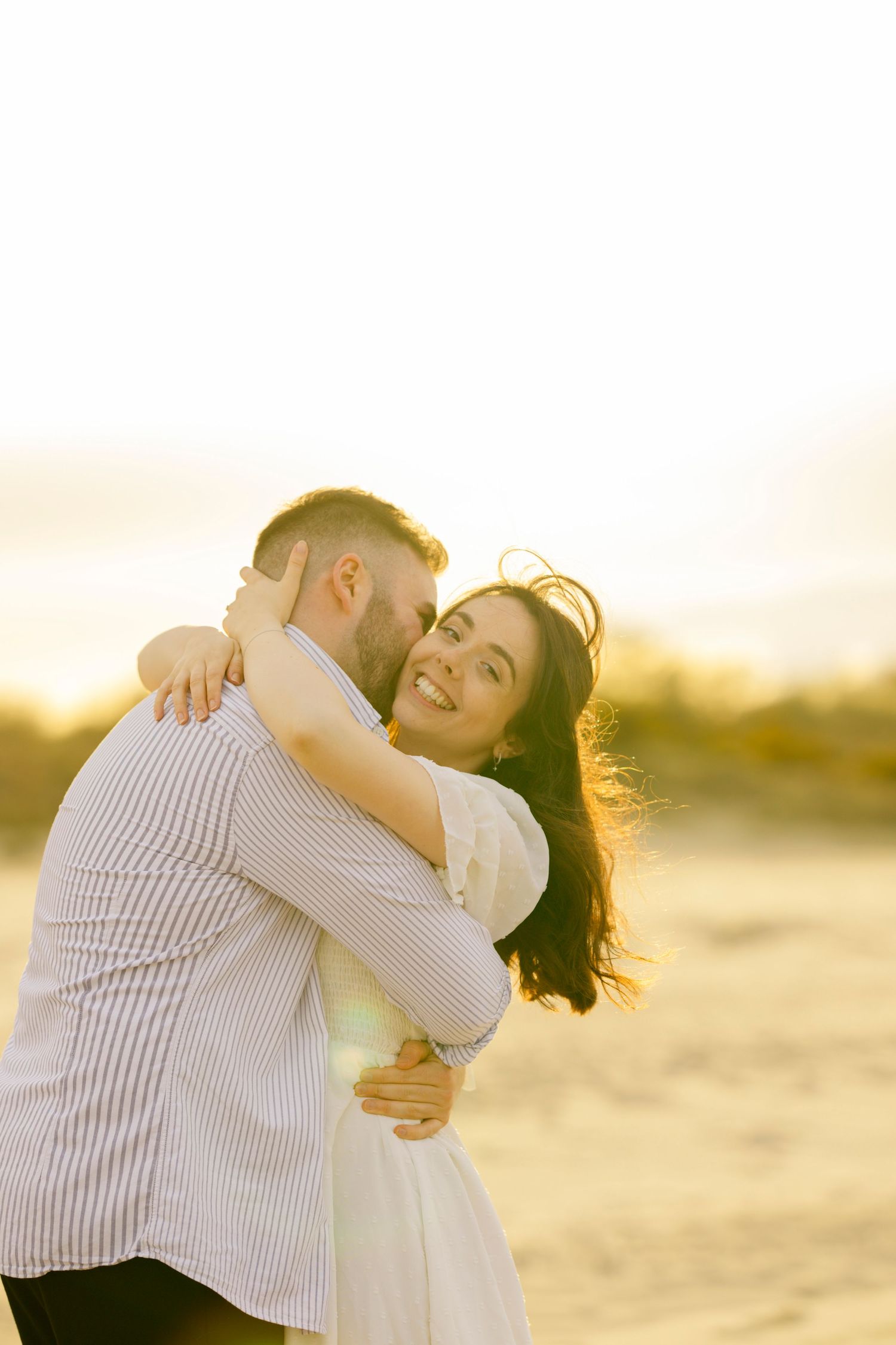 Romantic couple embraces during golden hour on sandy beach.