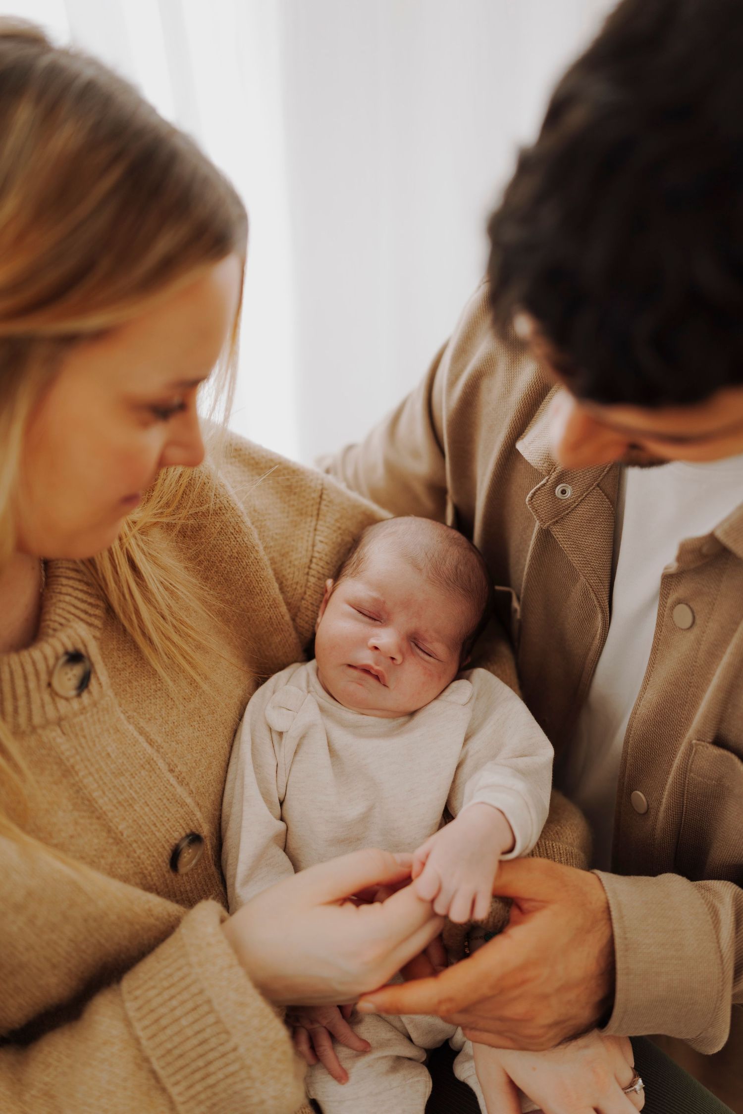 Tender moment between parents and newborn baby captured in warm tones.