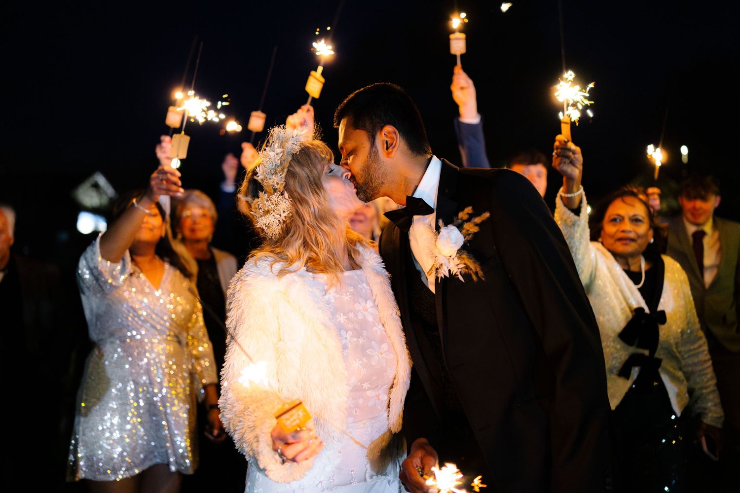 Wedding couple embraces during sparkler exit celebration at night.