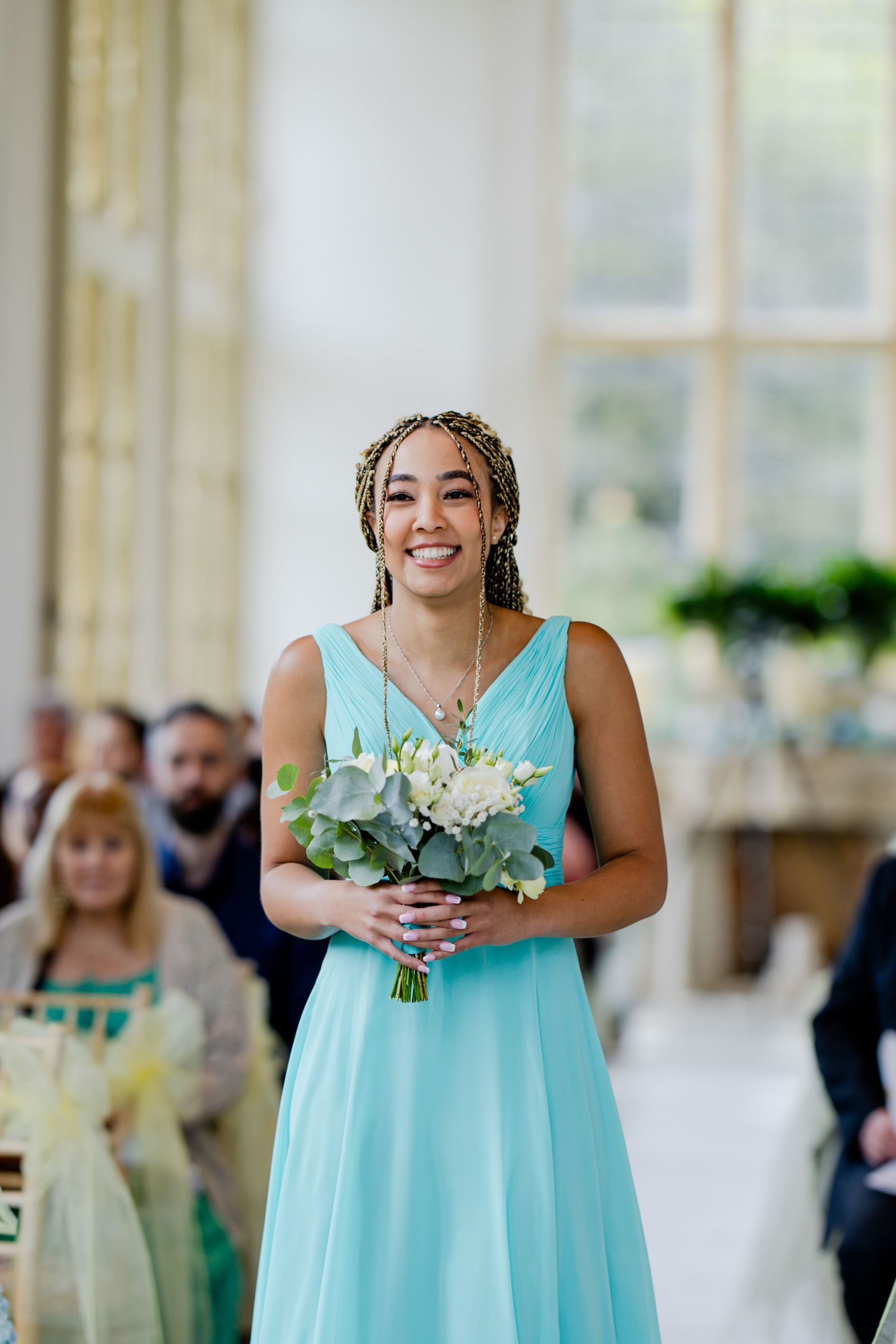 A bridesmaid in a turquoise dress holds a bouquet of white flowers and greenery.