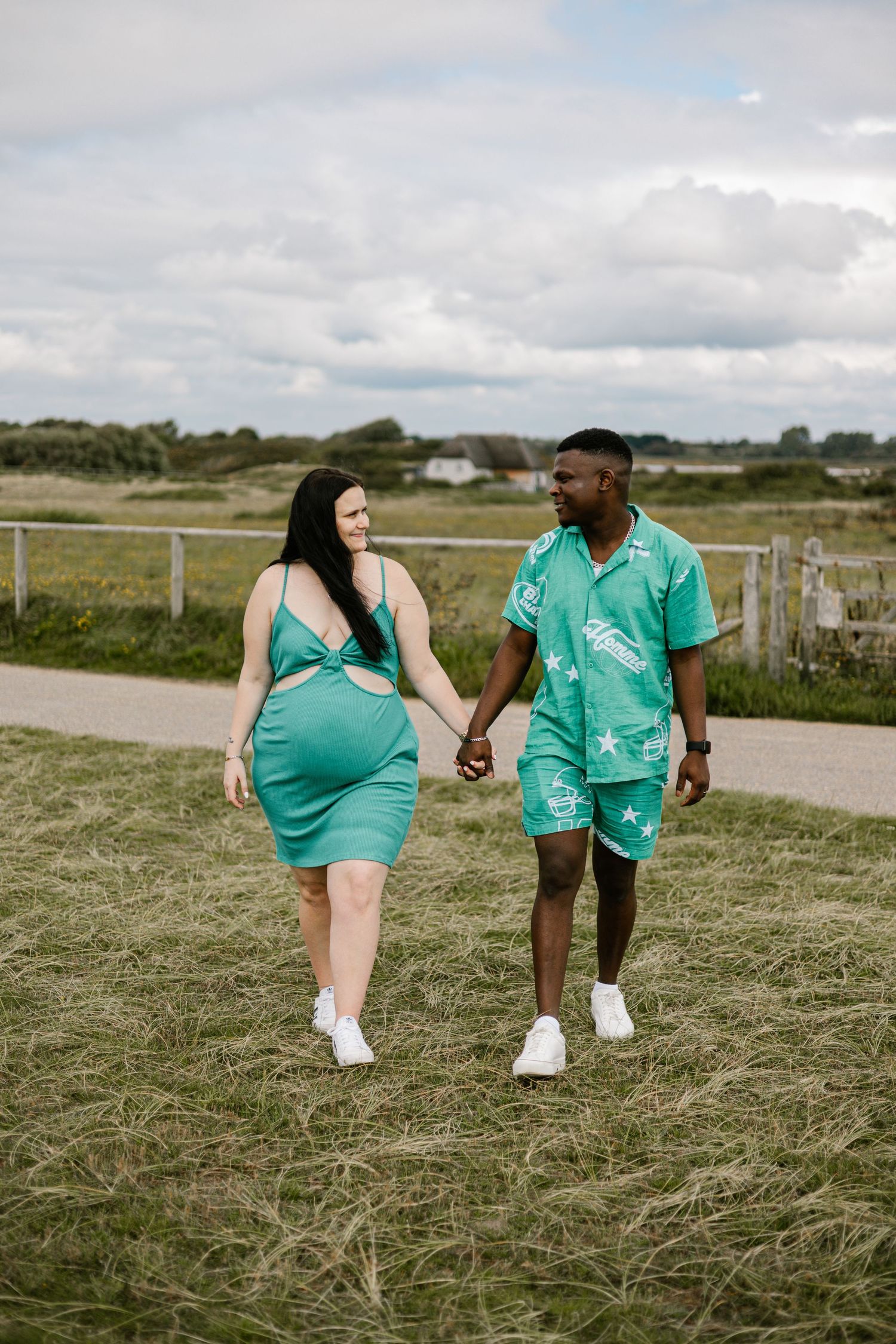 A couple in matching teal outfits walking together on a path through a grassy field.